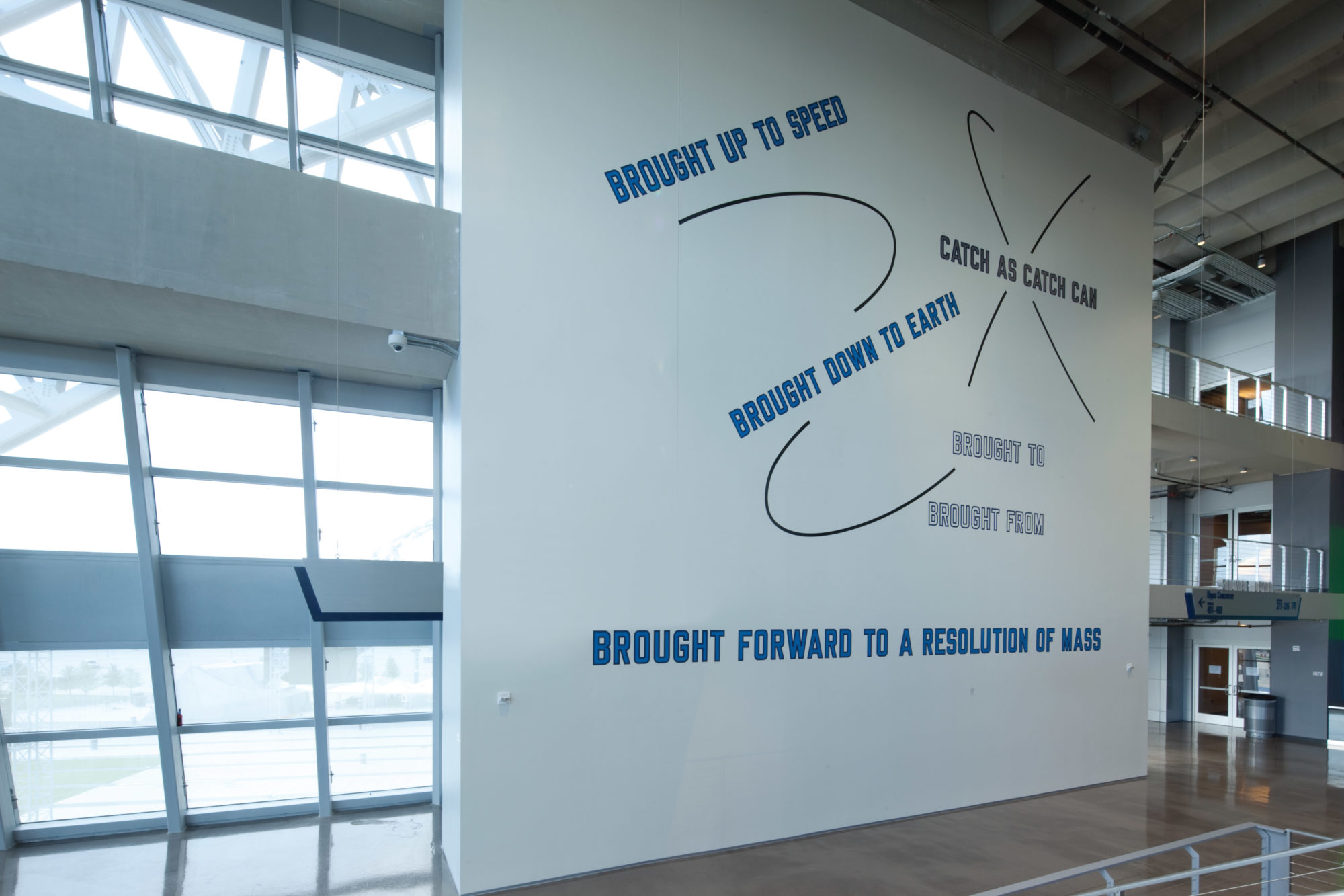 Blue vinyl text is displayed on a large wall in the Southwest Monumental Staircase of the AT&T stadium. The text reads, 