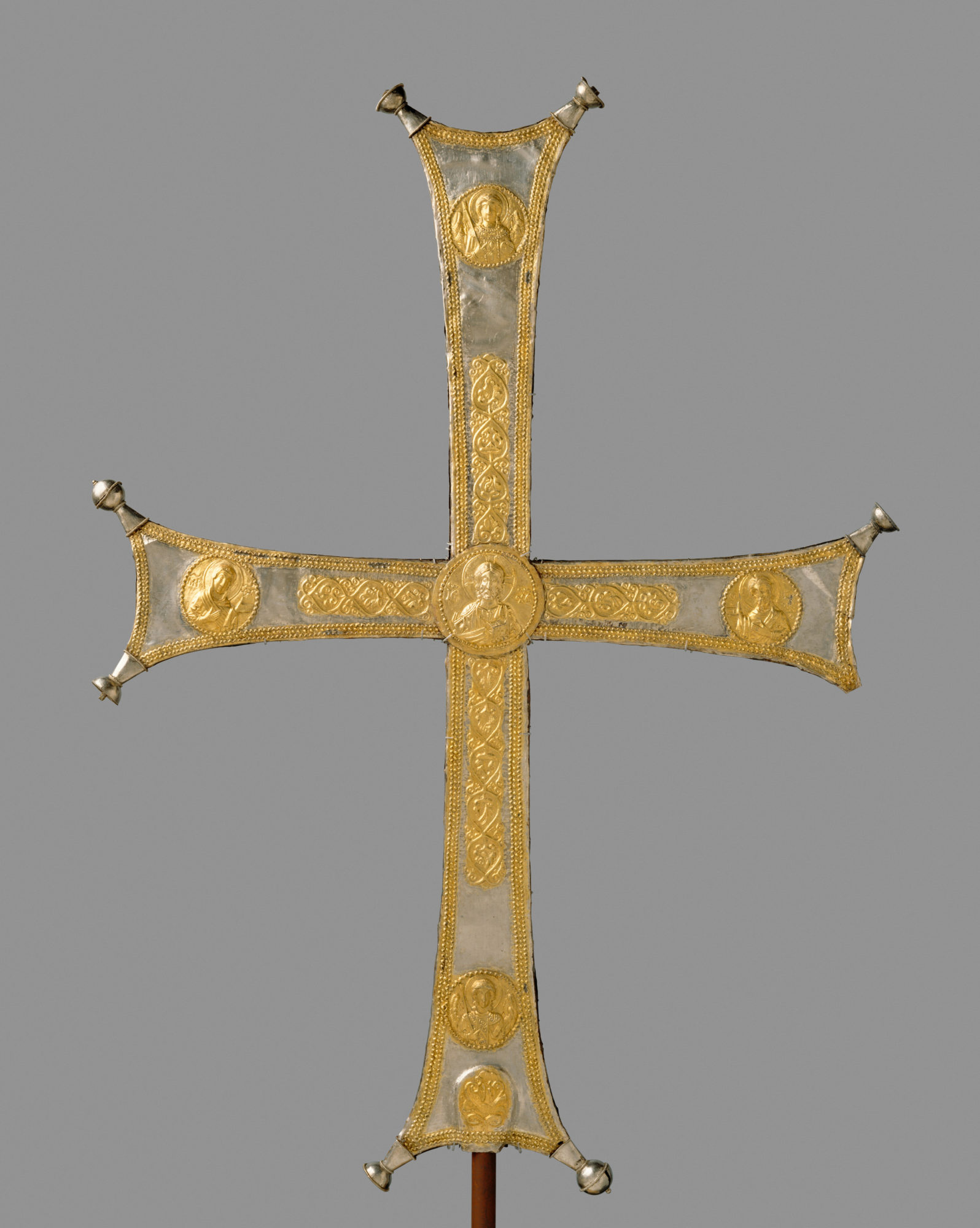 gold-embellished cross on a pole with small circular portraits against a gray background