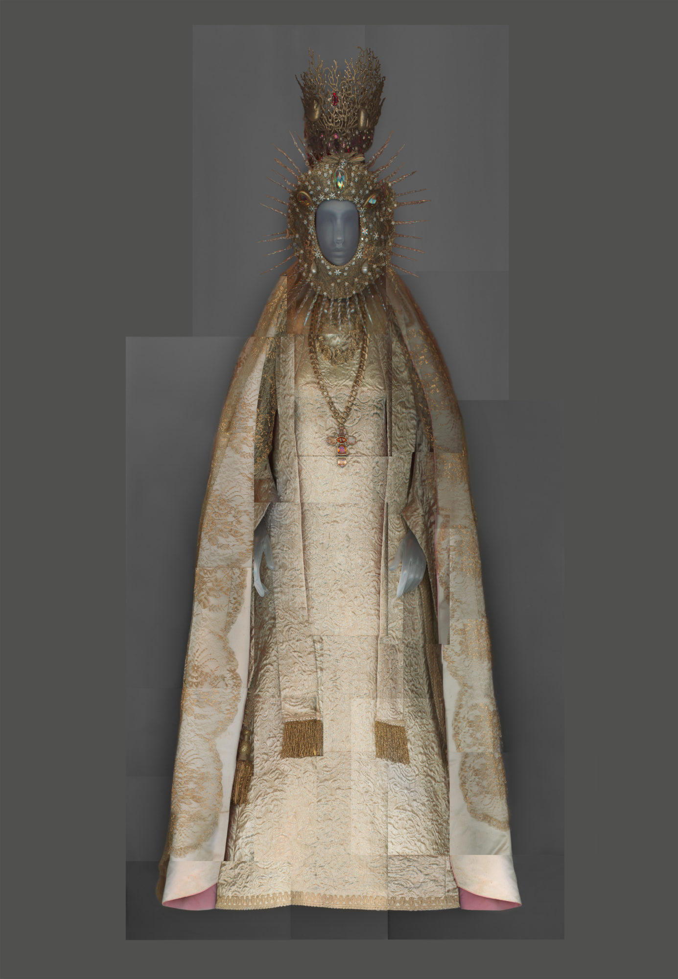 gold, shiny gown with tassels, a robe, a large golden cross necklace and headwear with golden spokes coming out from around the face.