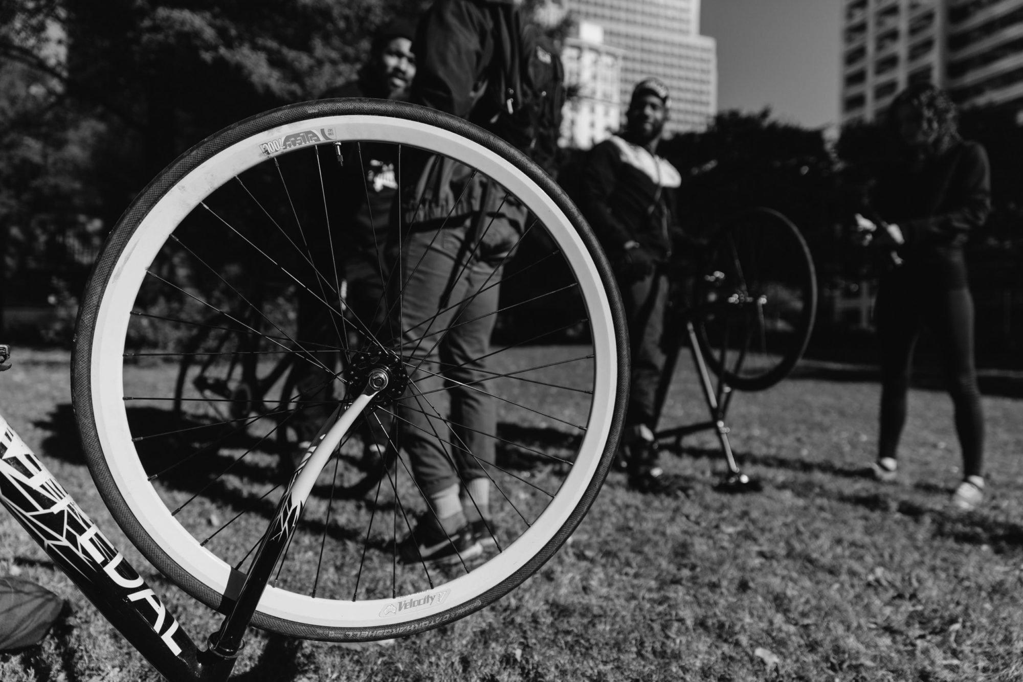 A black and white photo of a bicycle wheel with four men standing behind it.