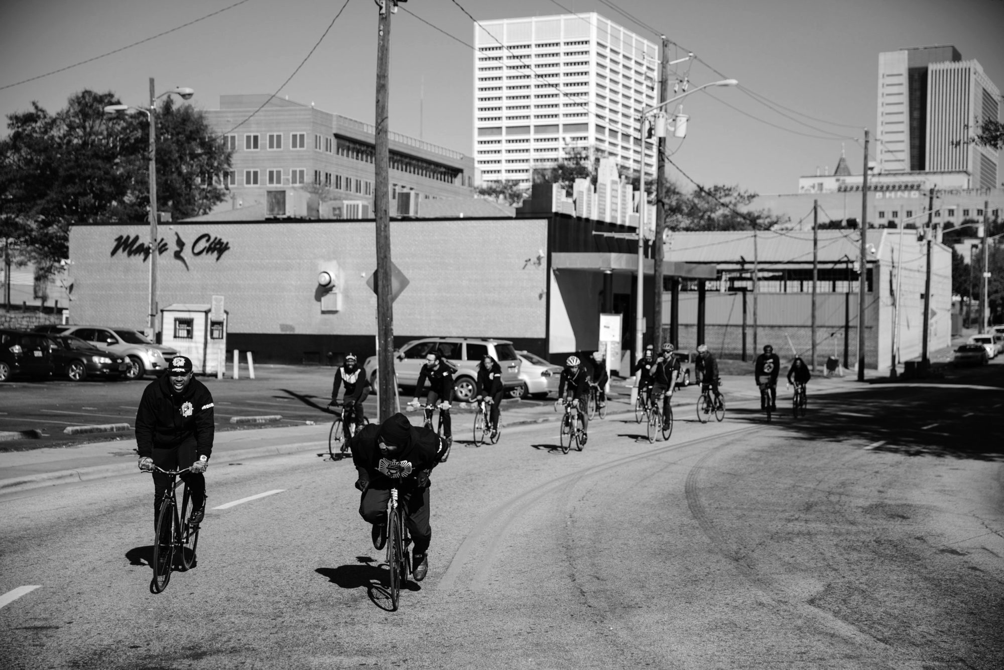 A black and white photo of a fleet of cyclist riding around a corner.