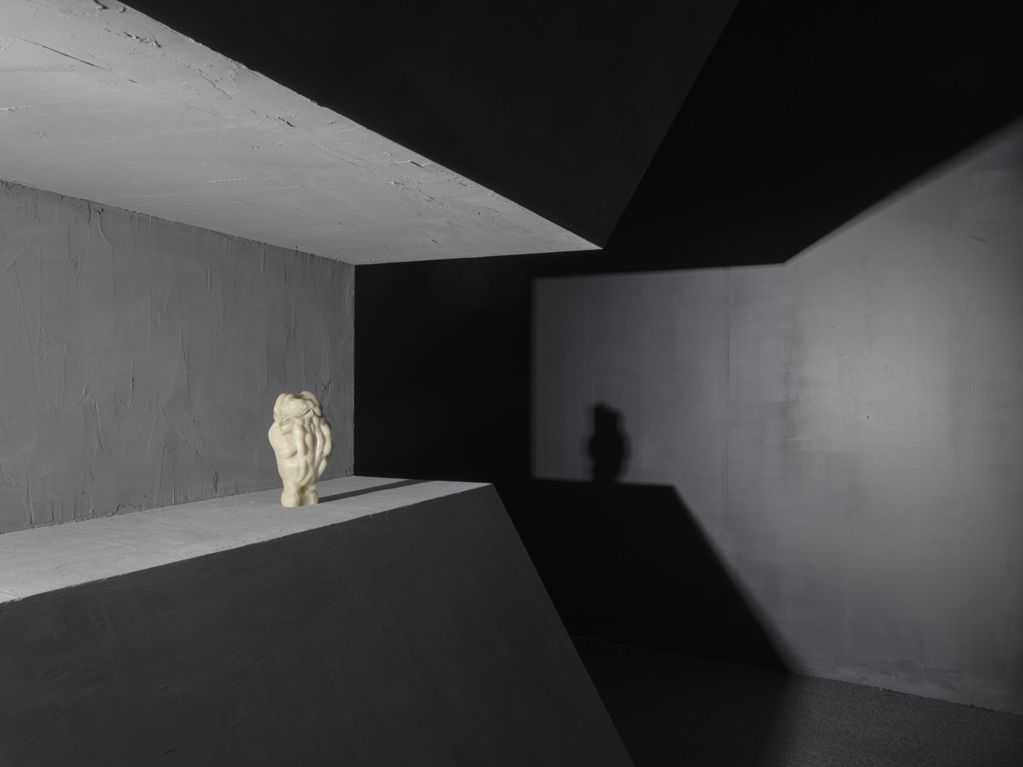 closeup view of small white figure greeting its shadow at the end of a carved gray space