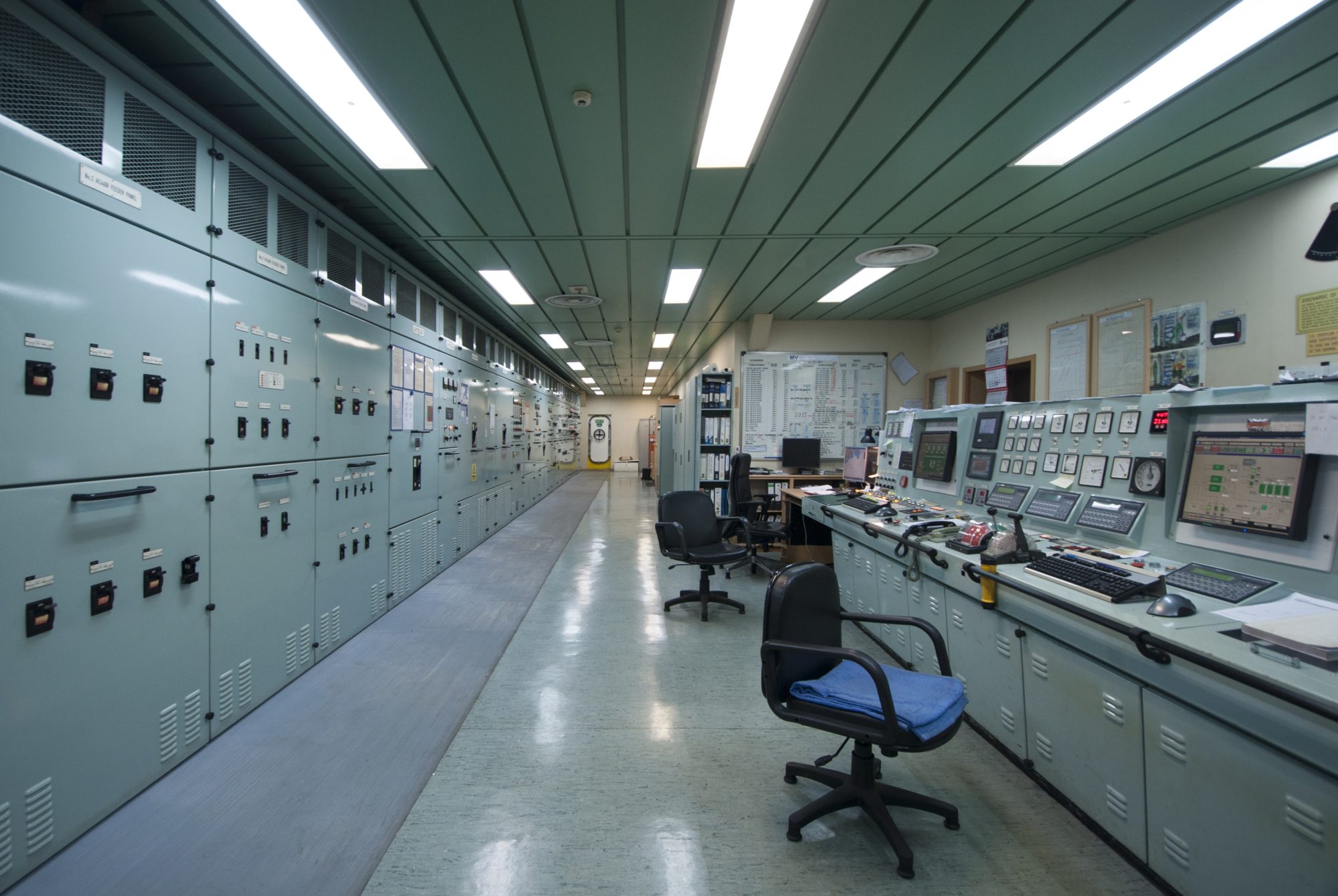 empty cargo ship control room complete with paneled ceiling, computers and file cabinets all uniformly aquamarine blue-green