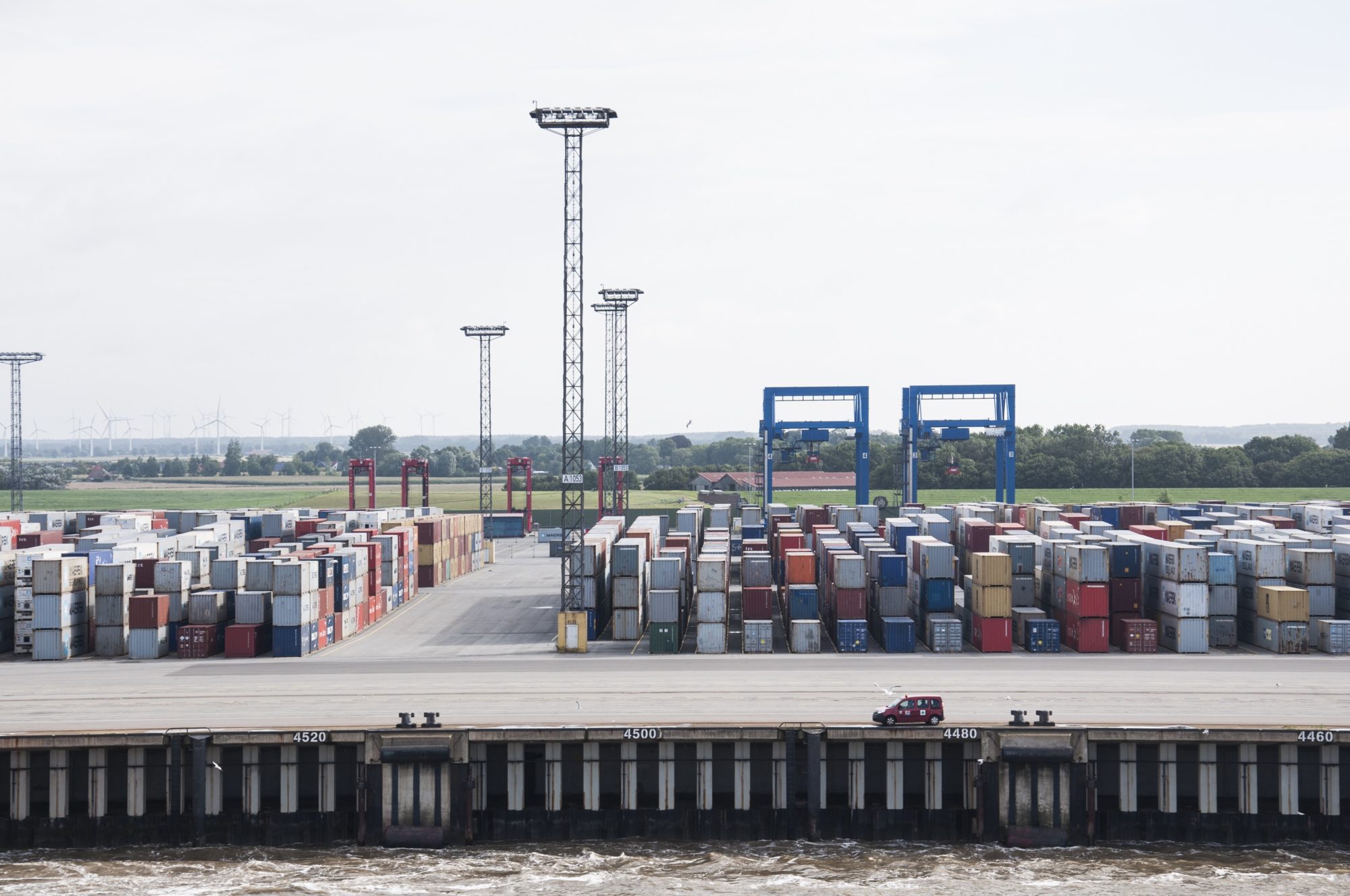 faraway photo of lone red car parked at the edge of a shipyard holding hundreds of containers