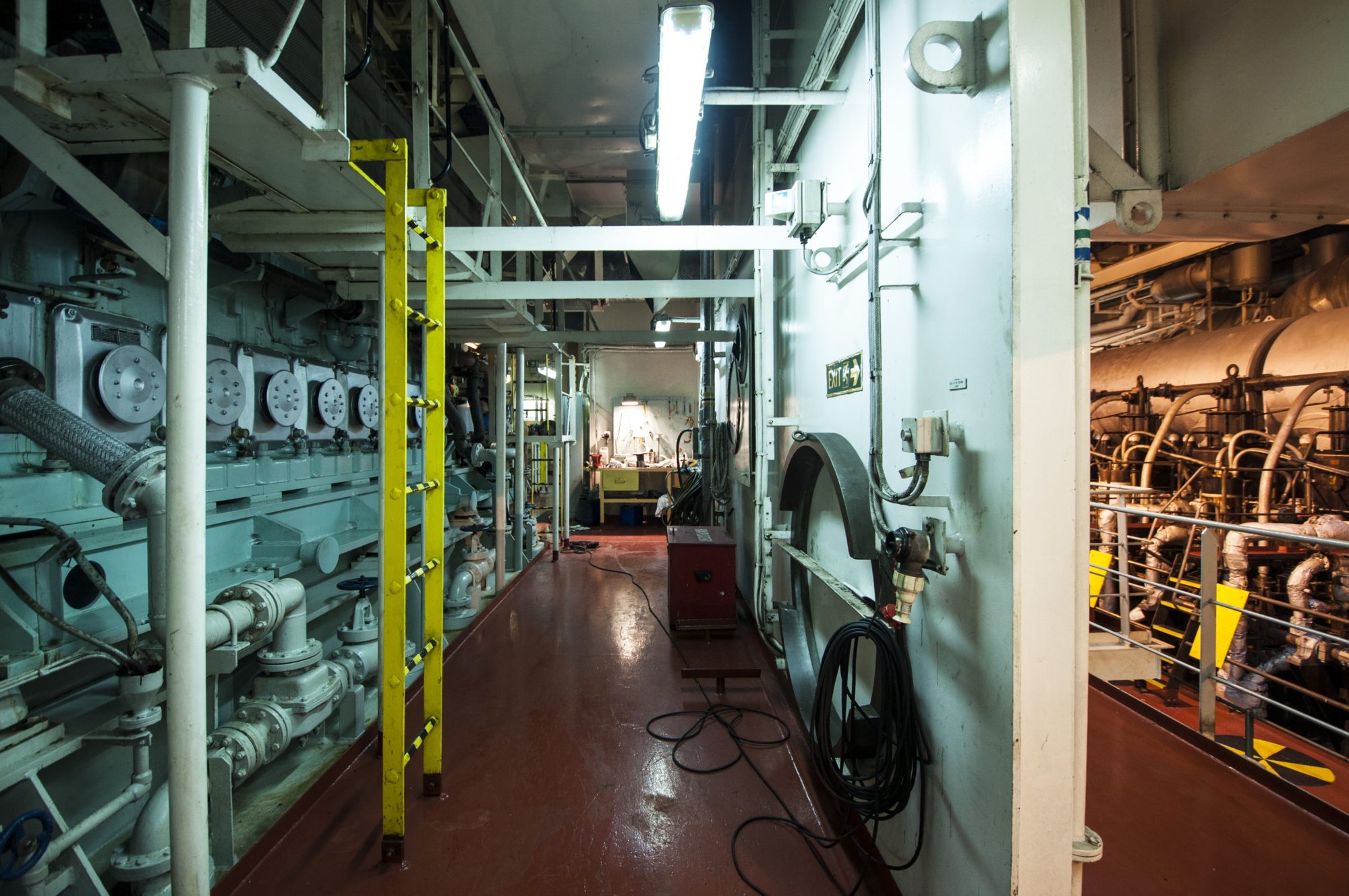 image of cargo ship bridge room; neon yellow ladder, caution signals and aquamarine pipes and walls visible