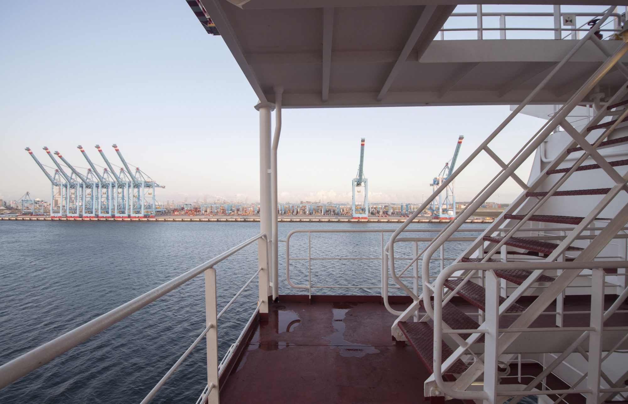 daytime view from lower deck of cargo ship of water and cranes along the shoreline