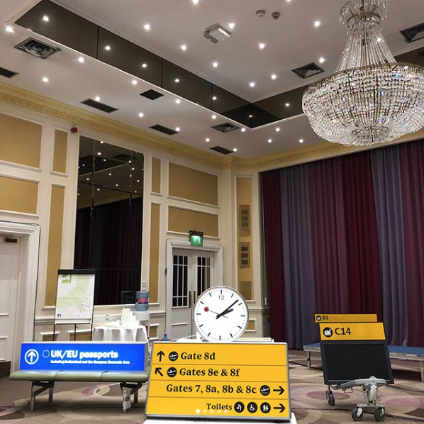 various airport signs in a ballroom/meeting room with a large timer and a chandelier overhead