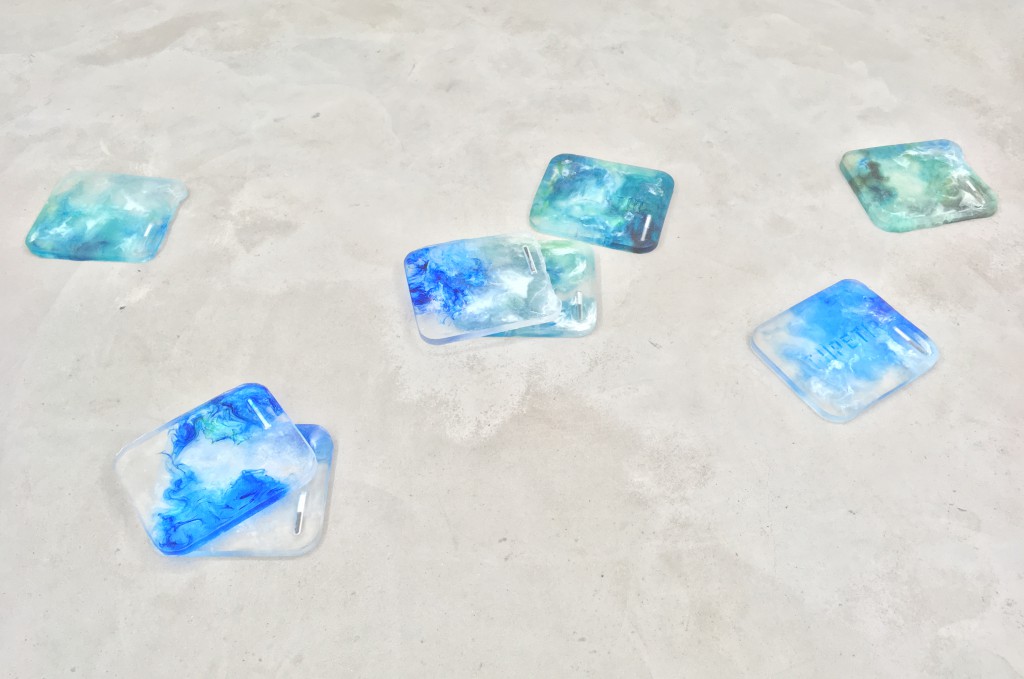 eight clear tiles with blue and green wave-like designs on sand