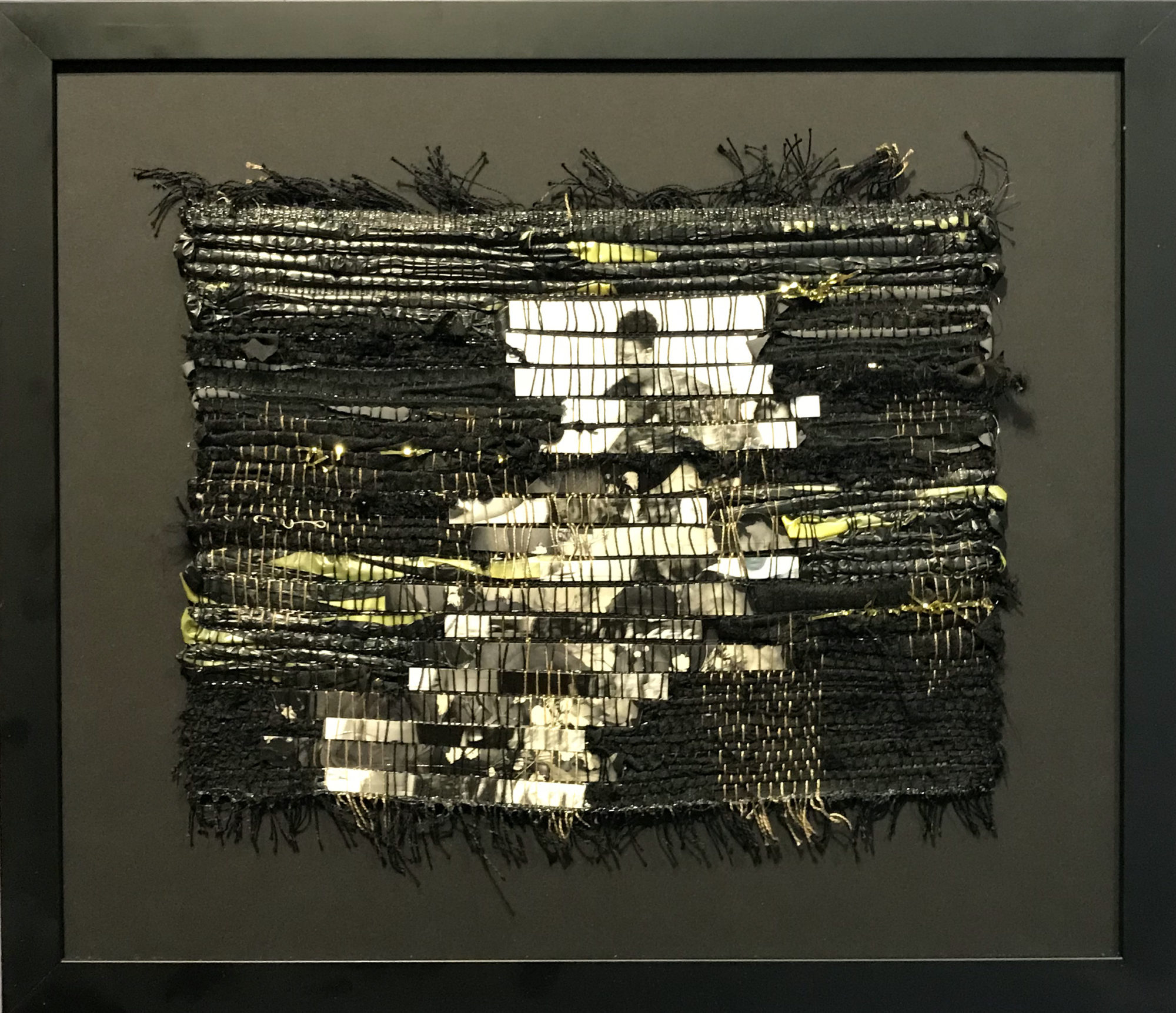 A rug-like patch, into which a photograph depicting human figures is woven, is attached to a black picture frame.