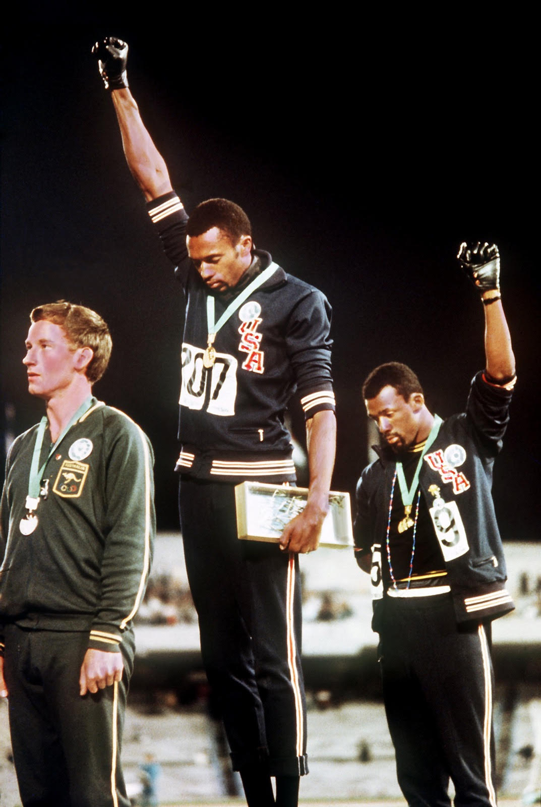 two of three figures receiving medals holding a fist in the air