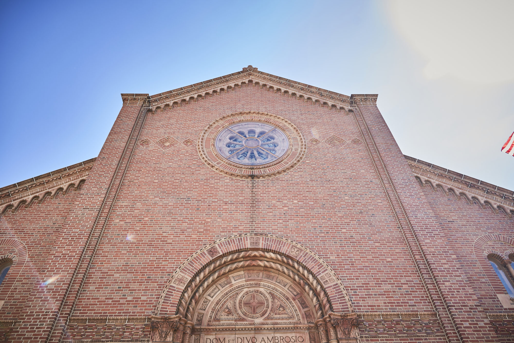front of a brick building with a circular stained-glass window. there is latin writing above an arched doorway.