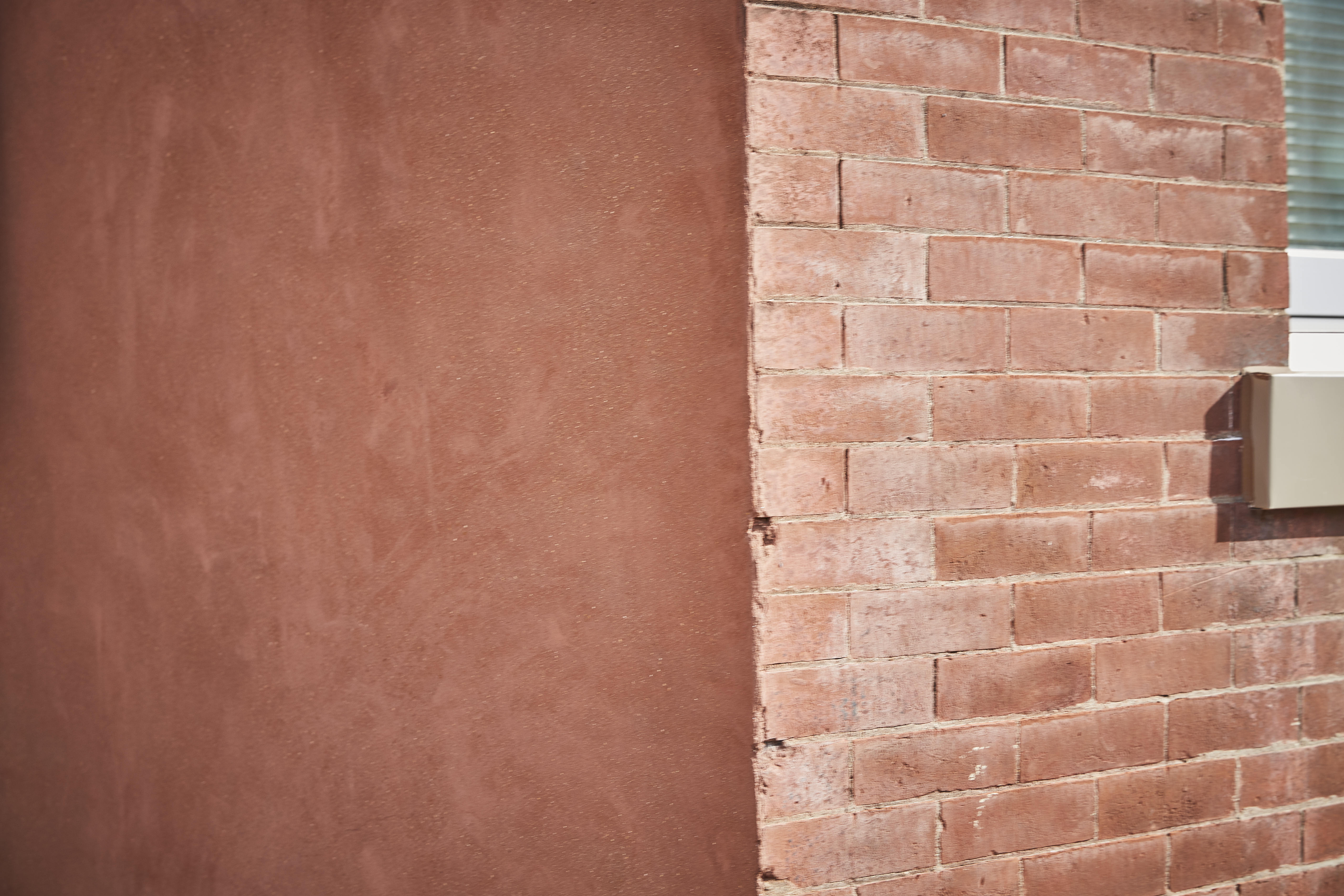 the corner of a brick building: one side is smooth and darker red, on the other, the intonations of the bricks are visible