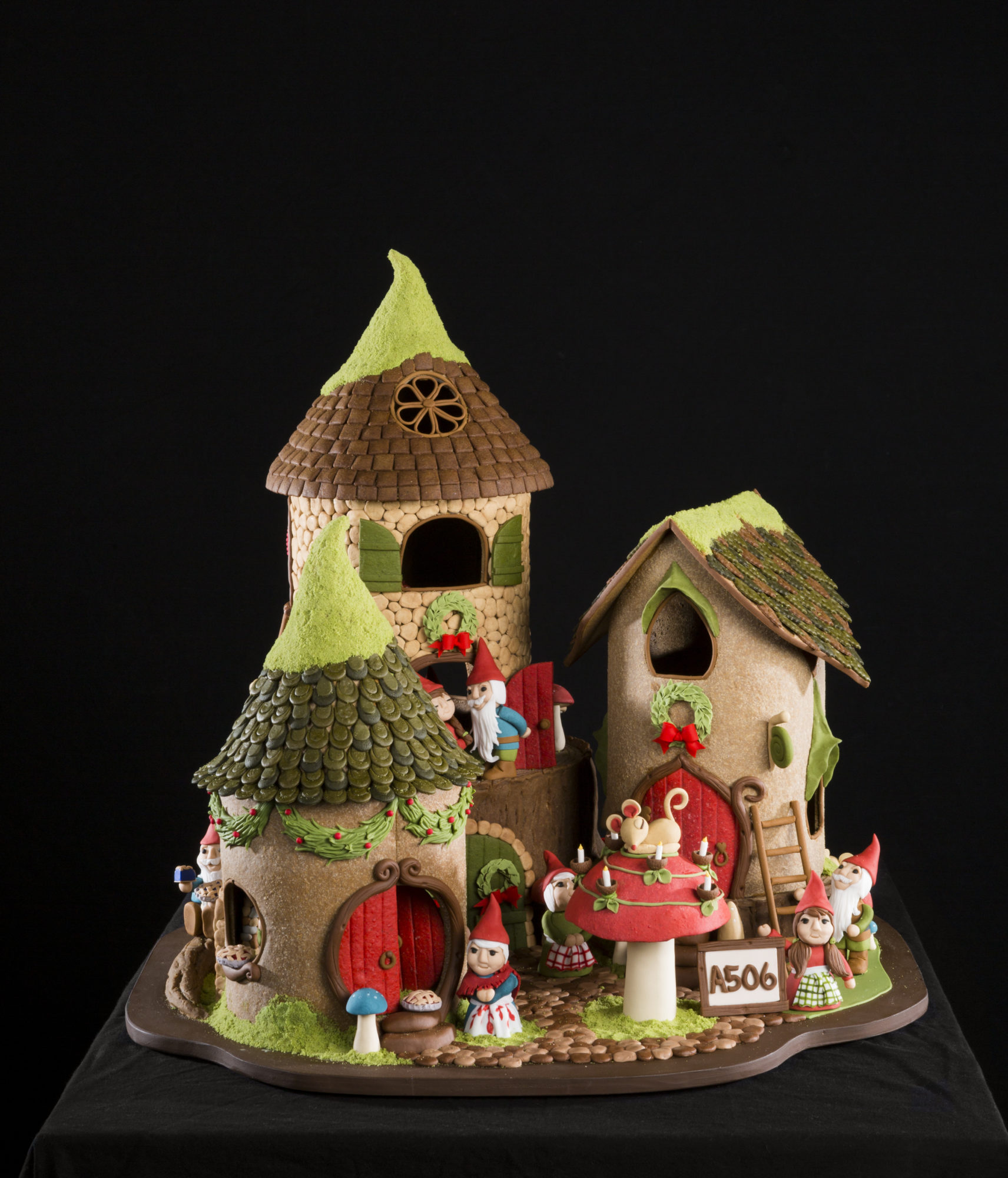 ornate gingerbread dwarf house with three sections of homes, mice, a ladder, and a mushroom.
