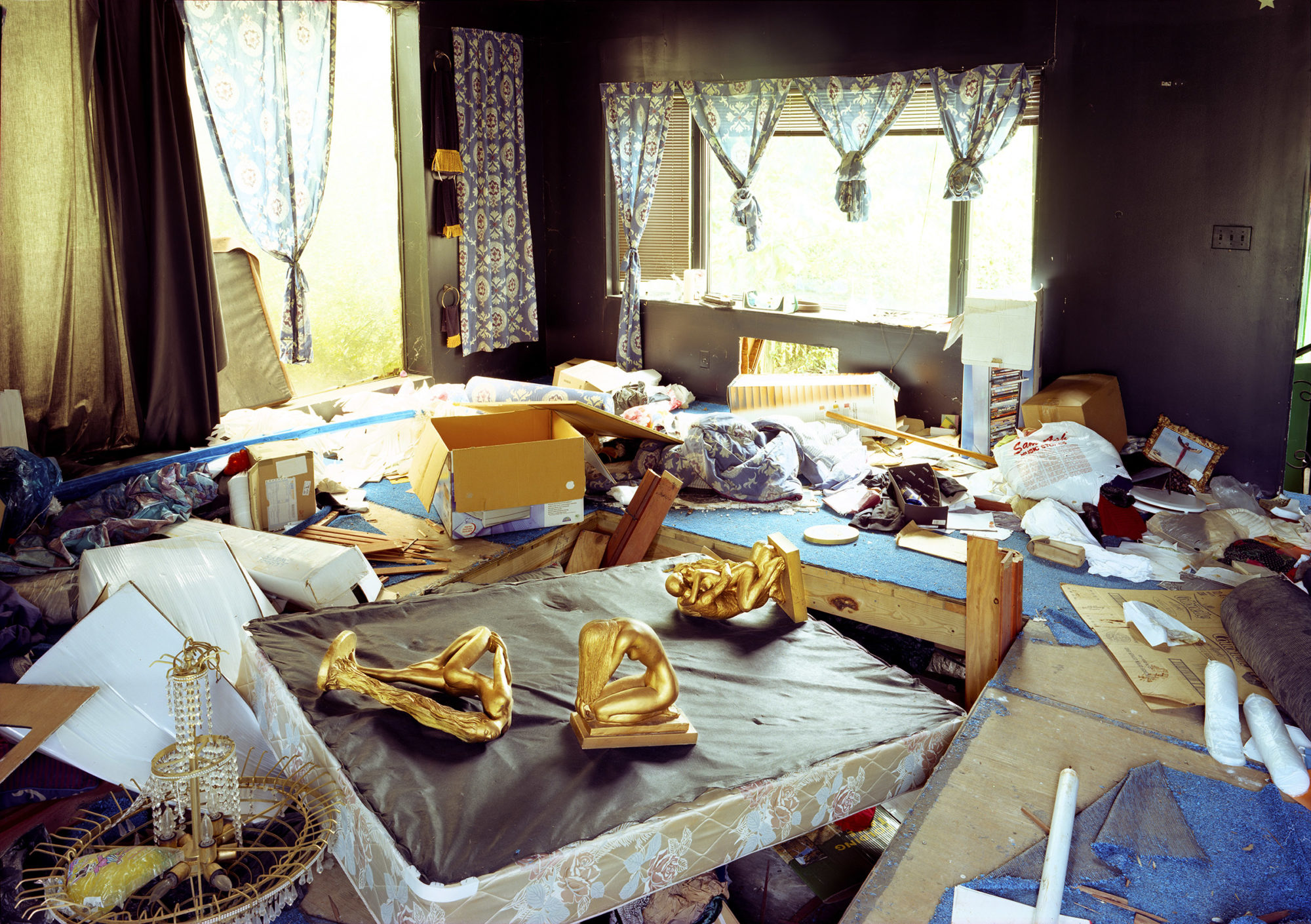 a room of mattresses. the mattresses are littered with junk--the one in the foreground features three golden statues, one of which is in a coital position