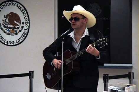 musician with a cream hat and dark suit performing with a guitar in front of a mircrophone