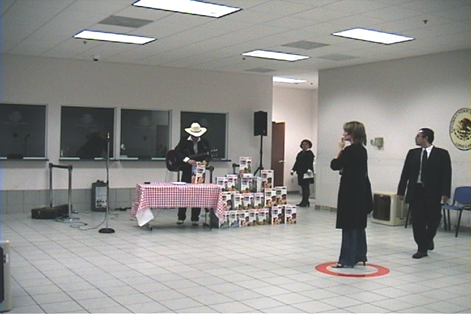 woman standing in a red circle on a tiled floor infron of a musician with many boxes of cereal