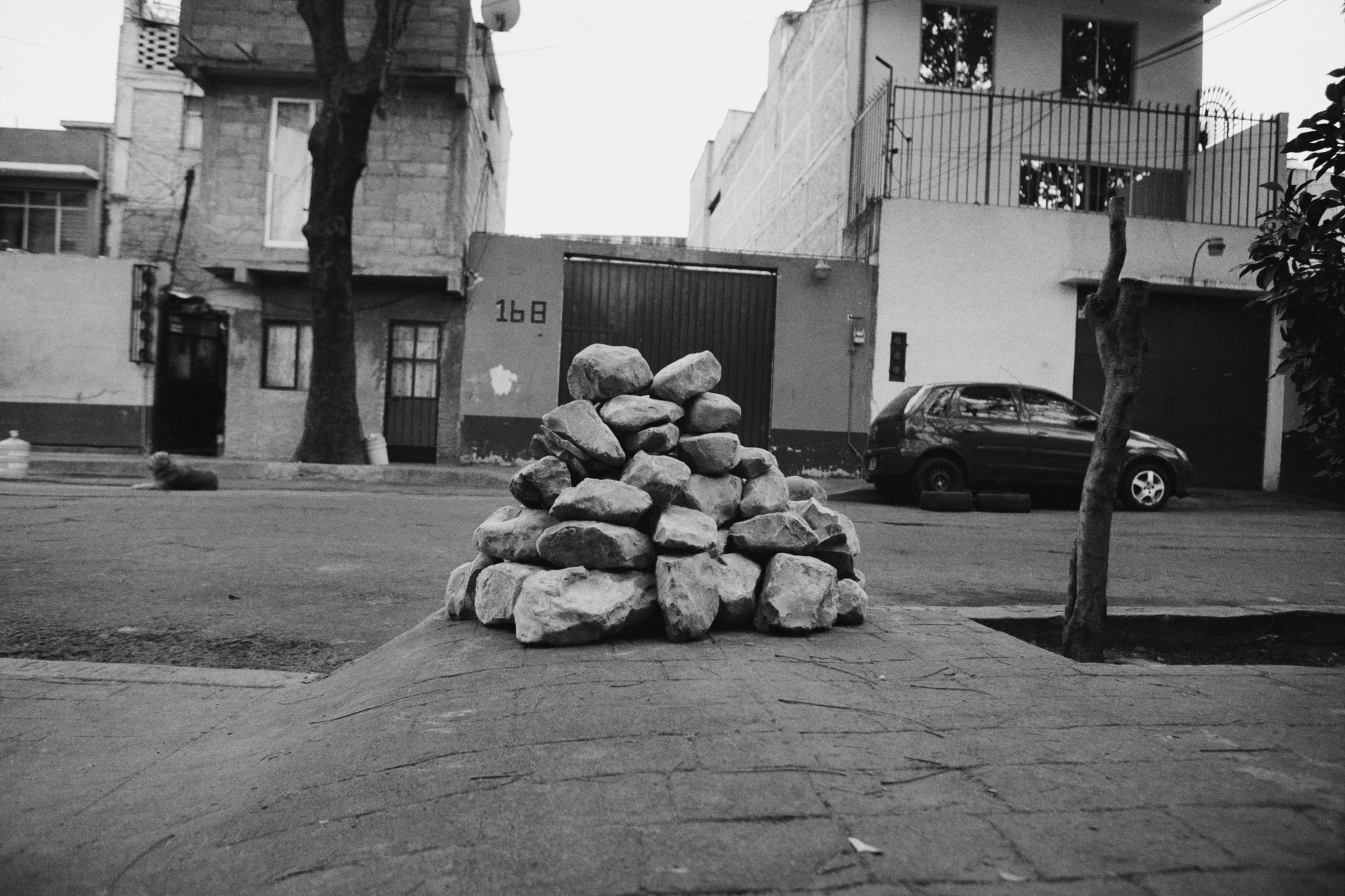 pyramid of rocks on the sidewalk next to the road with a van parked on the curb