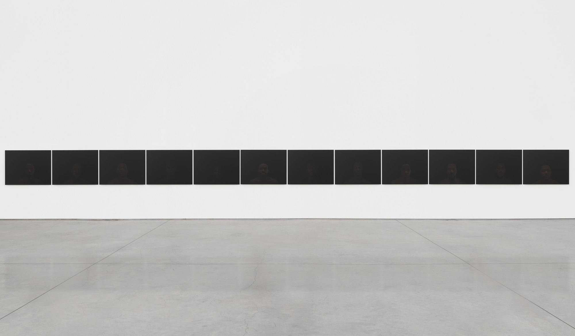 Twelve dark digital photographs on archival paper mounted on dibond hanging side by side on a gallery wall