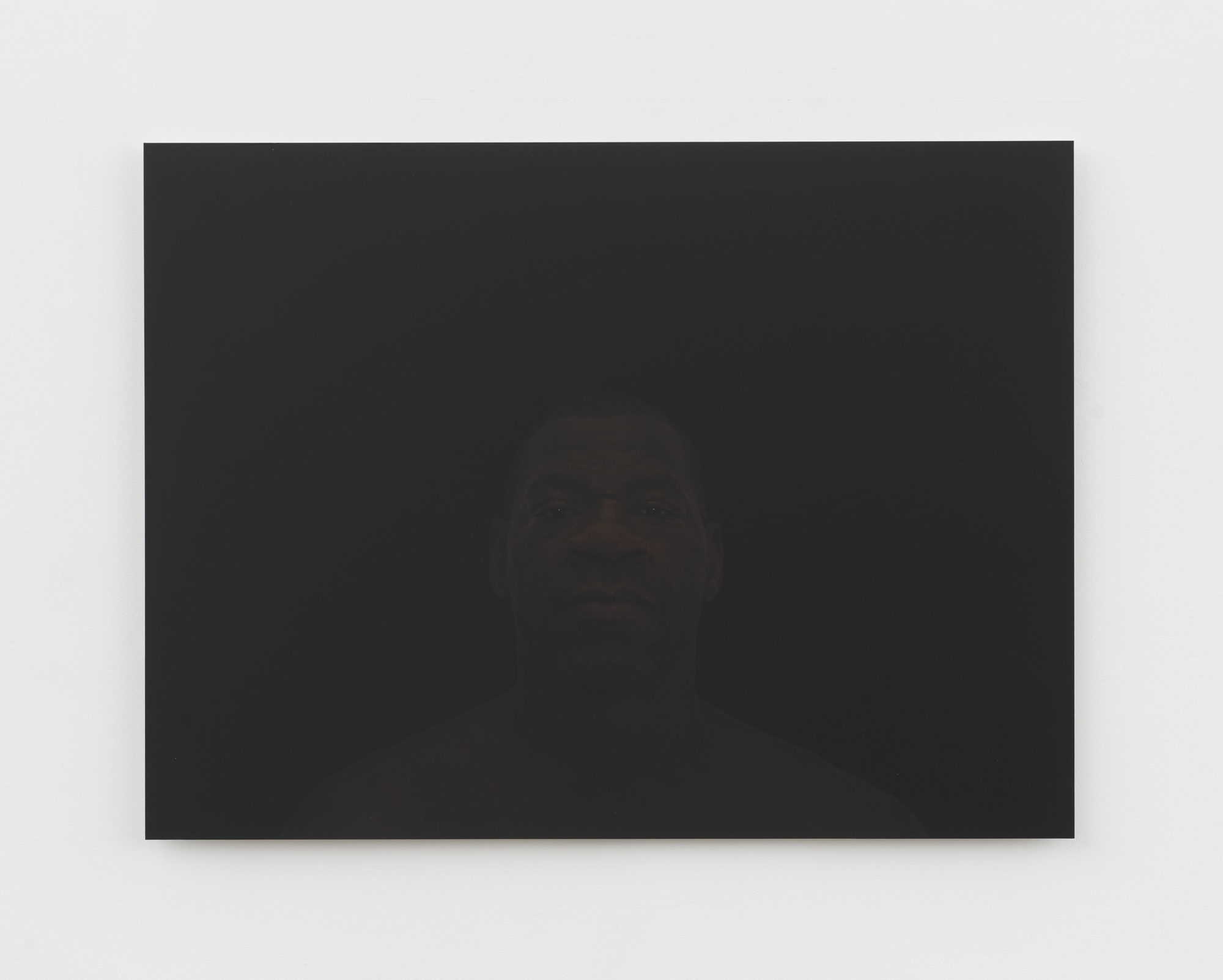 A straightforward portrait photograph of an older black man in front of a black background