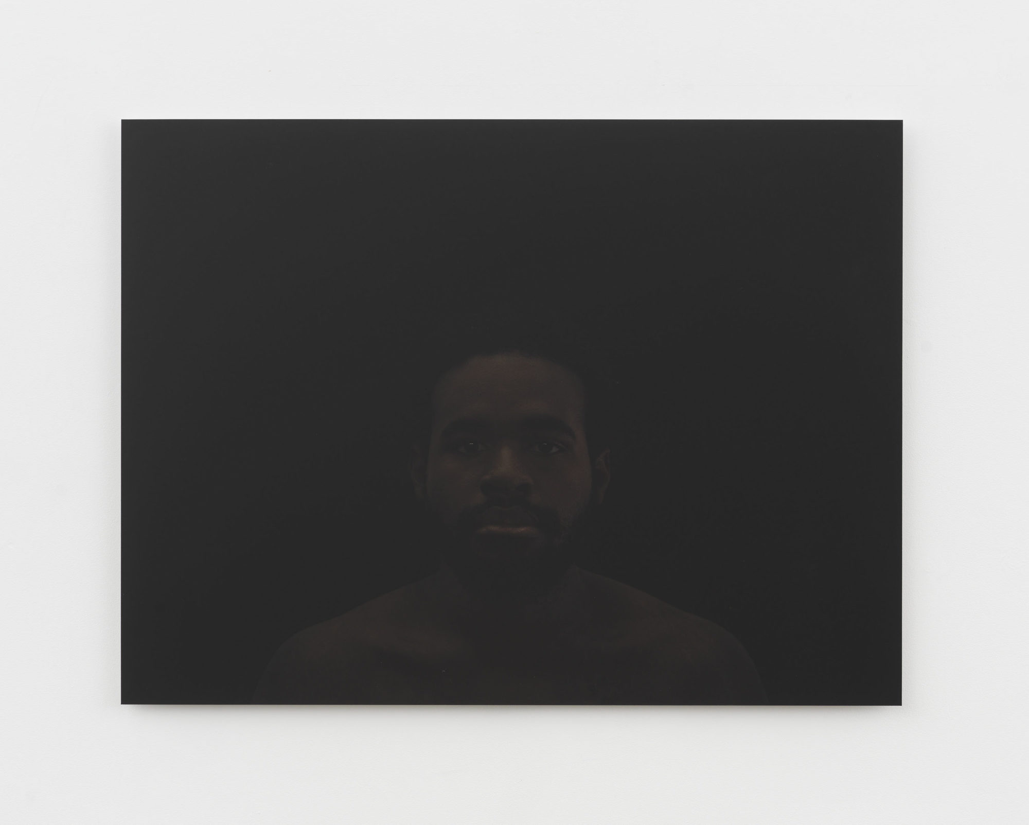 A straightforward portrait photograph of a bearded, black man in front of a black background