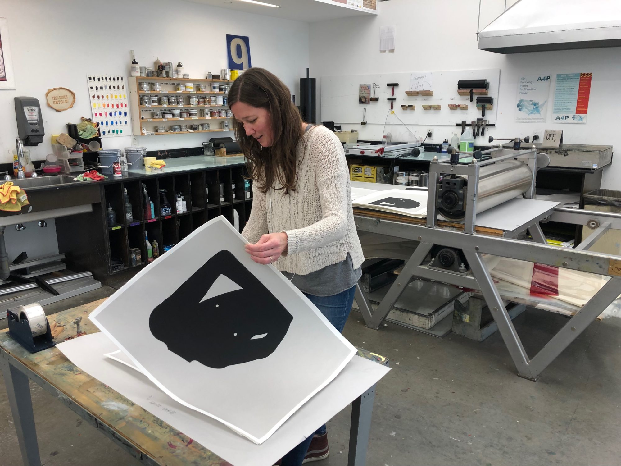 Woman in white sweater flipping through large prints in a printmaking studio