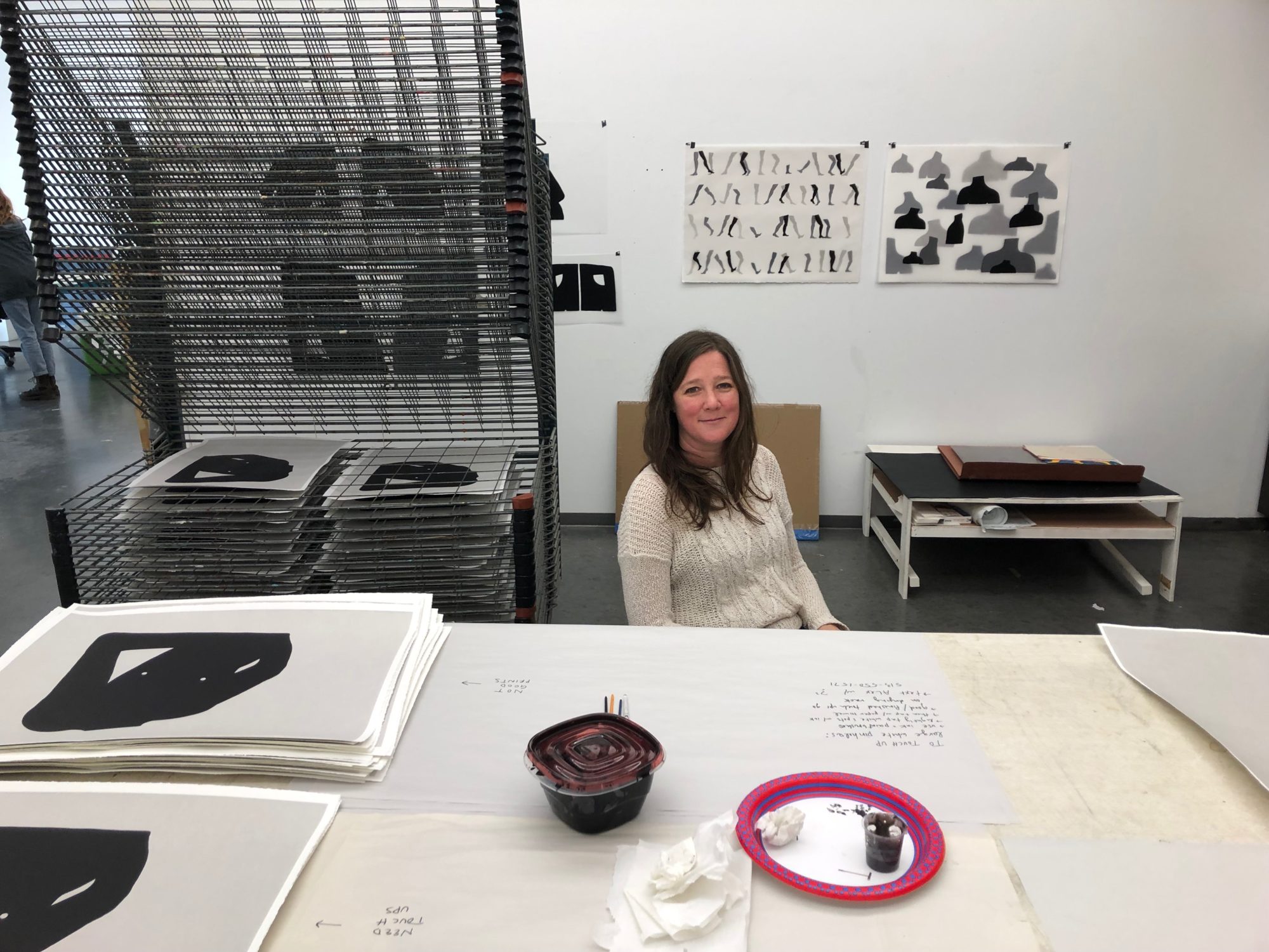 Woman in a white sweater sitting at a desk in a printmaking studio