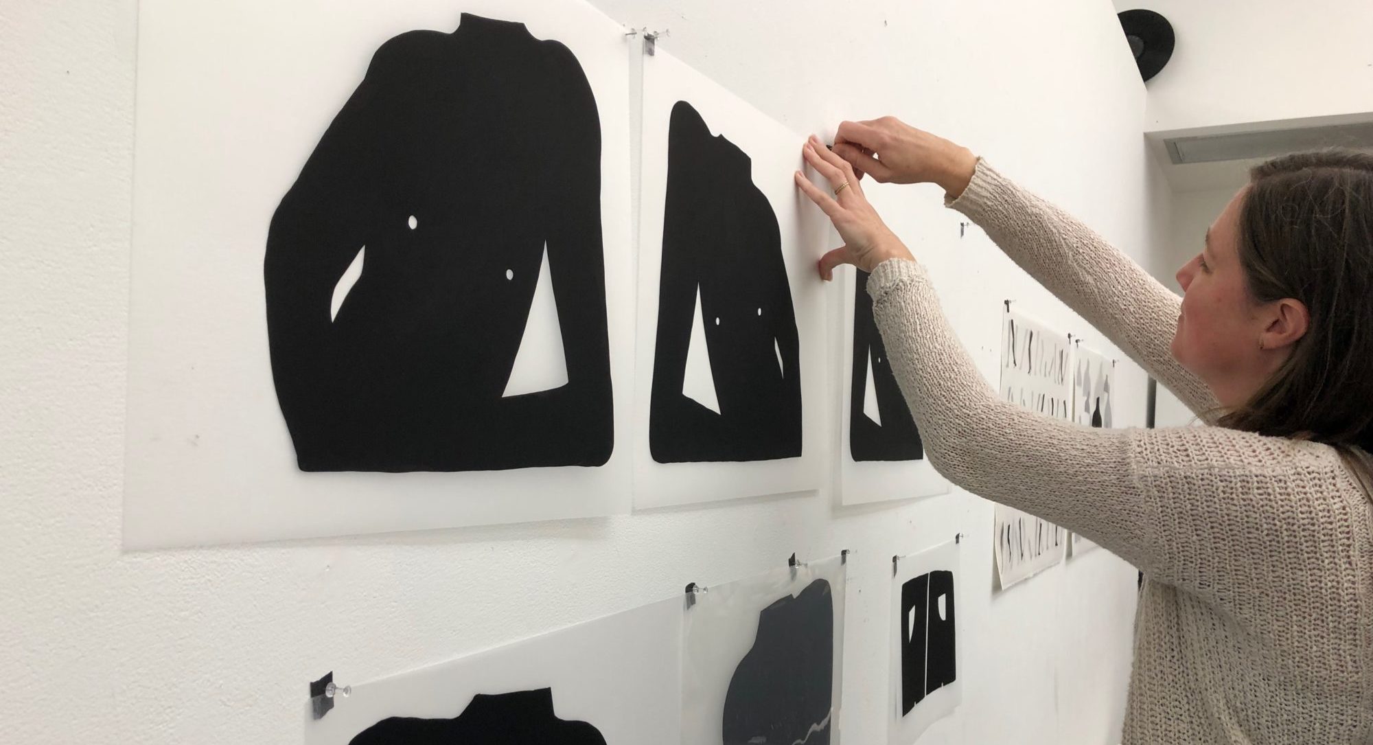 Profile view of a woman hanging a print on a wall in a printmaking studio