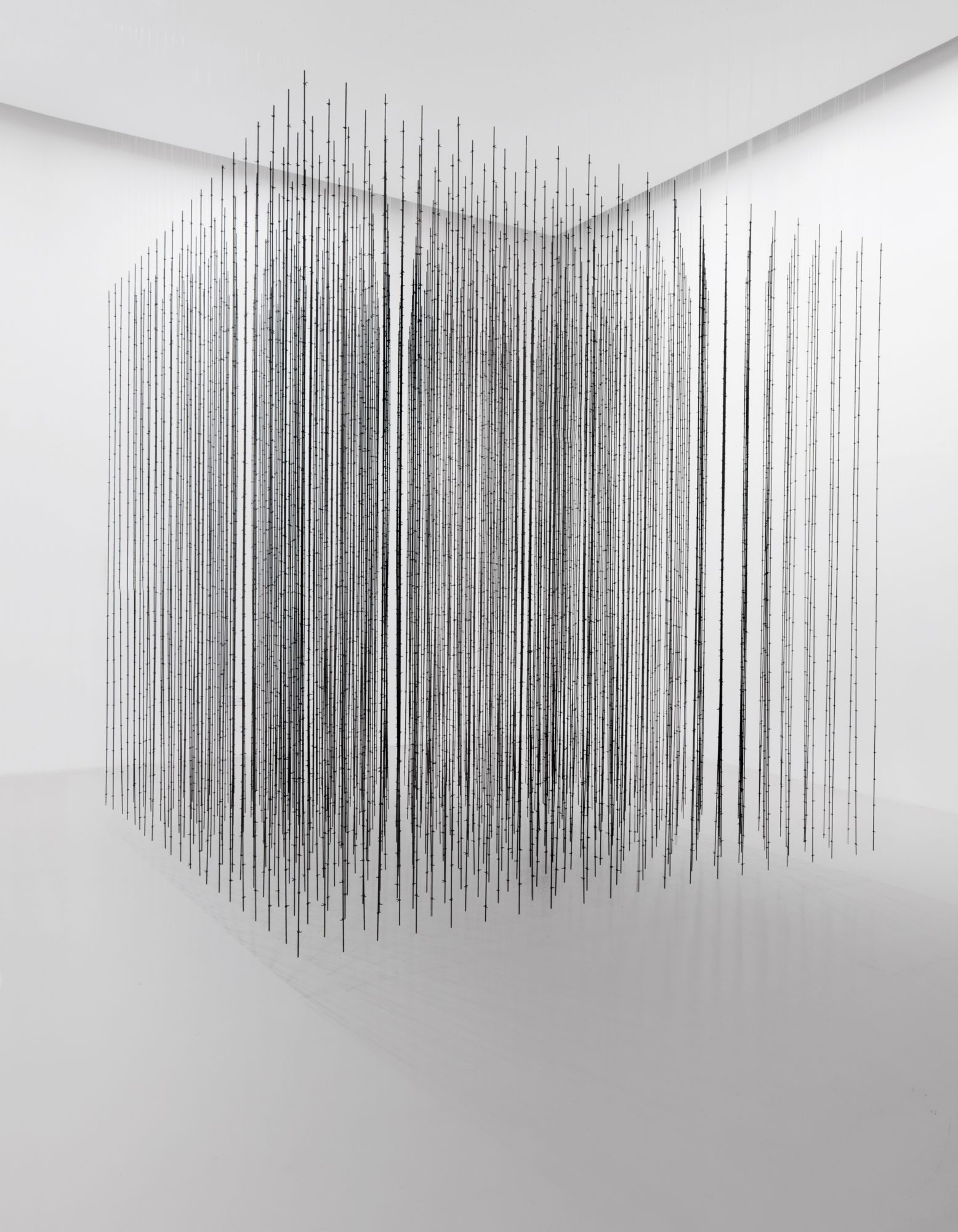 Hanging rows of black steel rods arranged into a square shape in front of a white wall