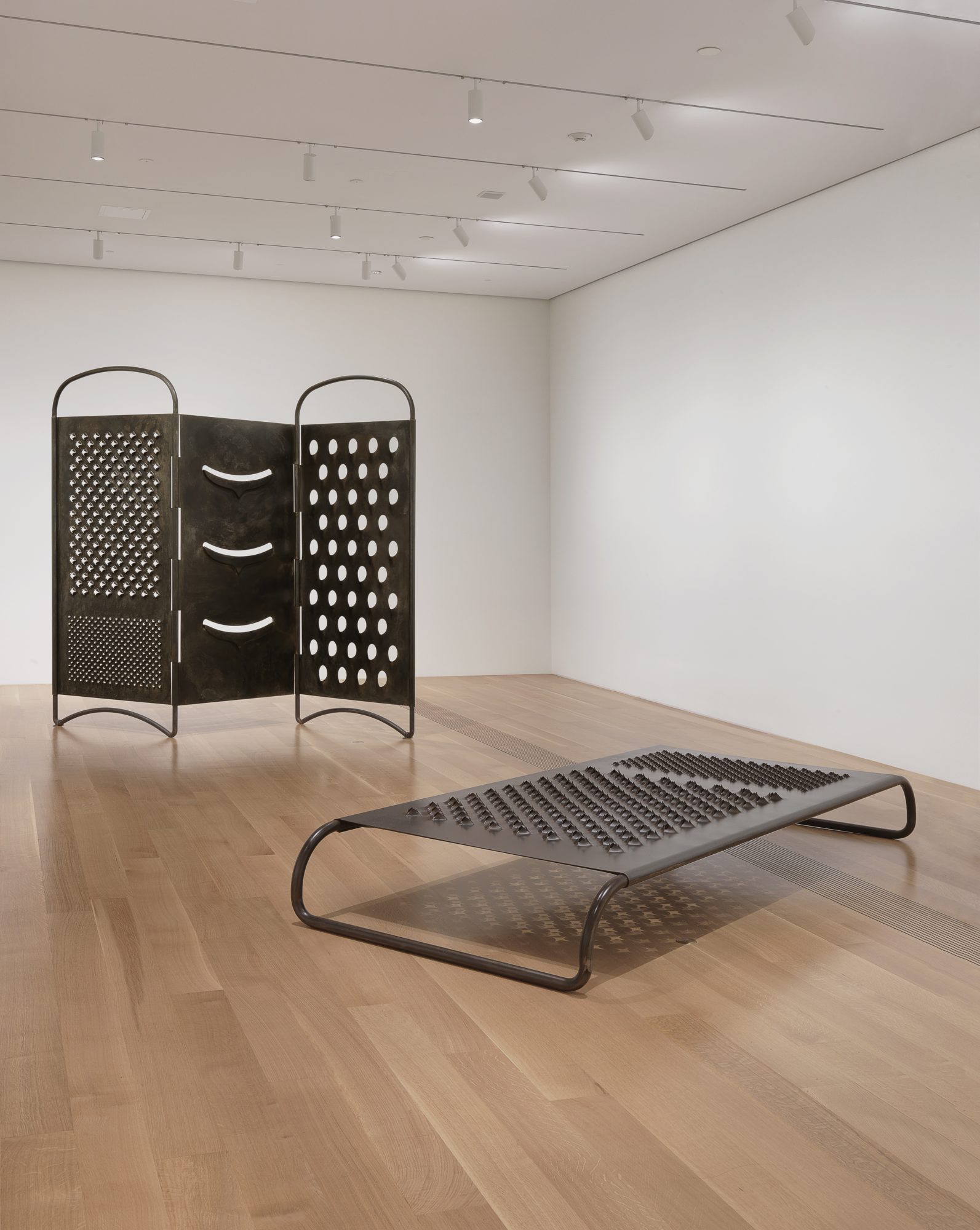 Gallery view of two large cheese grater-like objects, one laying on handles and one standing upright