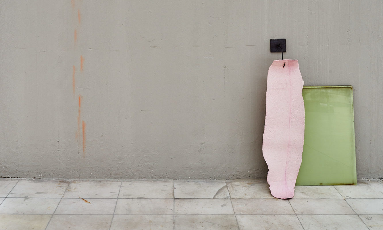 flat pink piece of rubber hung by small black hook, in front of green rectangular board up against a gray wall and on tile floor