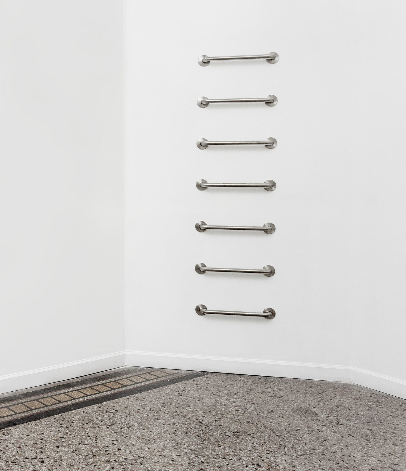 A vertical stack of horizontal metal grab bars is mounted on a gallery wall.