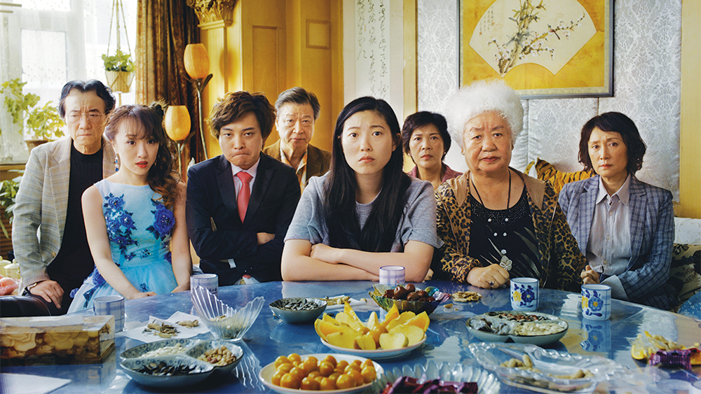 an Asian woman seated at a table covered with fruits and nuts surrounded by members of her family