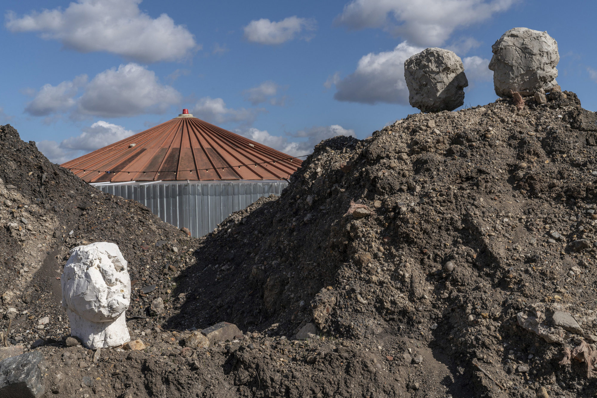 view of mounds of dirt with three rock structures of heads and a clear blue sky in the background