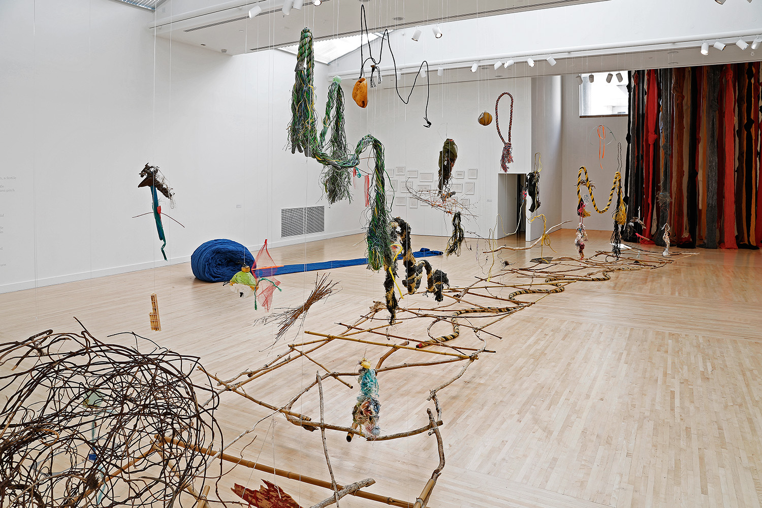 Installation view of Cecilia Vicuna's exhibition displaying a long, connected sculpture leading to a tall curtain of fabric in the background