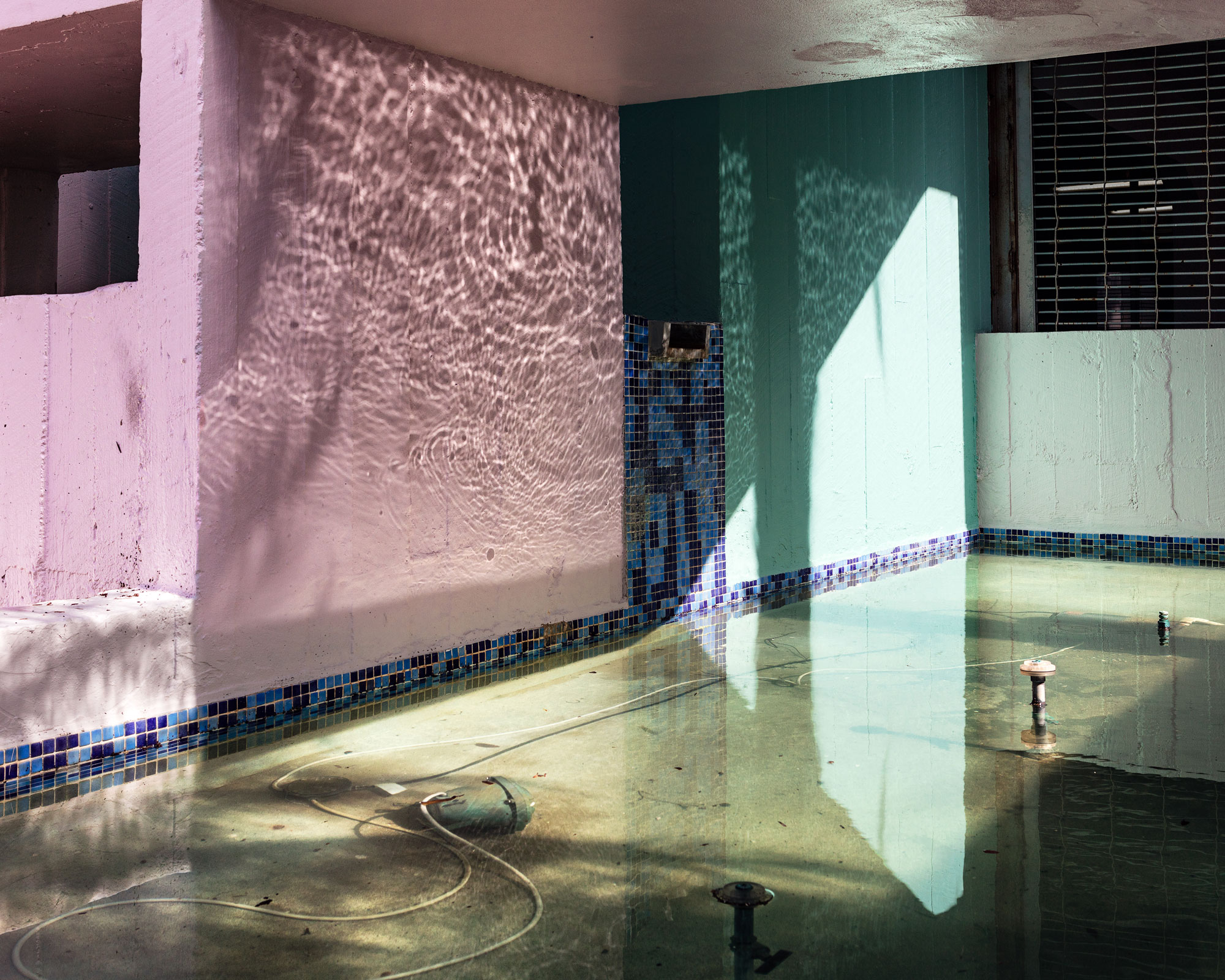 Photograph of abandoned fountain, water reflecting on pastel-colored walls.