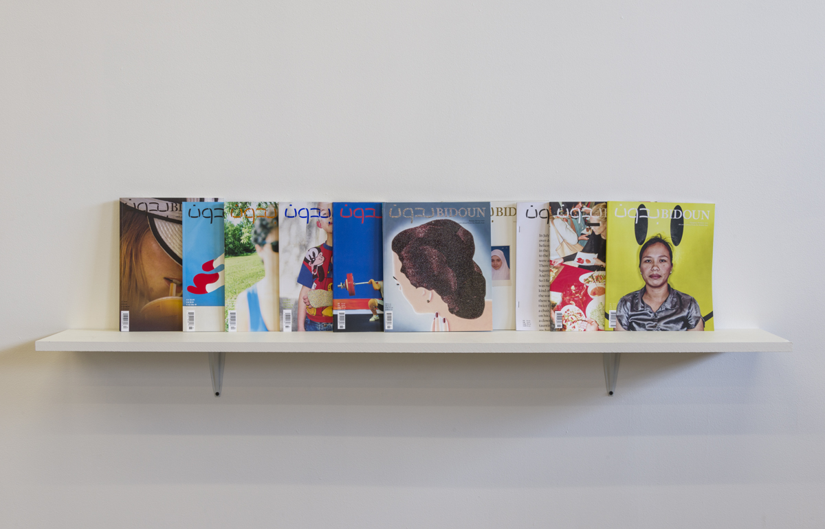 A series of magazines are lset standing up side-by-side on a white shelf