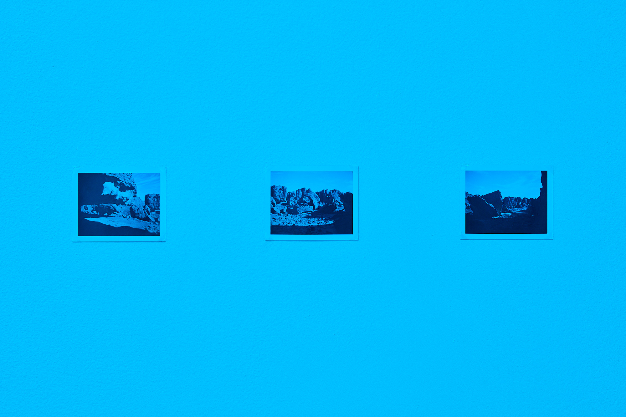 three image of rocky formations in bright sunlight hang side by side on the wall in a blue-tinted room
