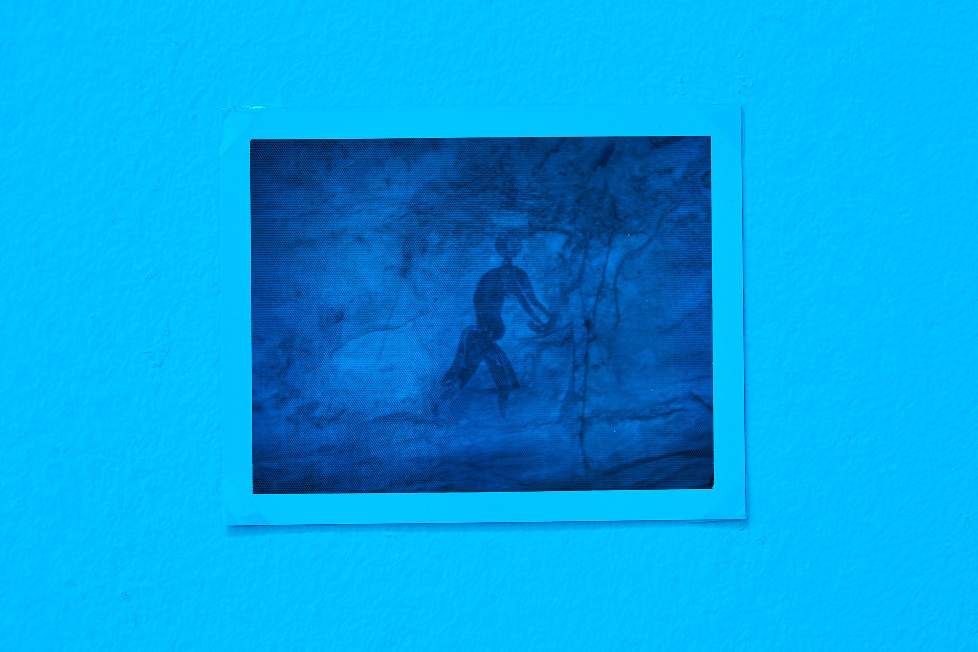 an image of what appears to be a primitive cave painting hangs on the wall in a room with blue tint