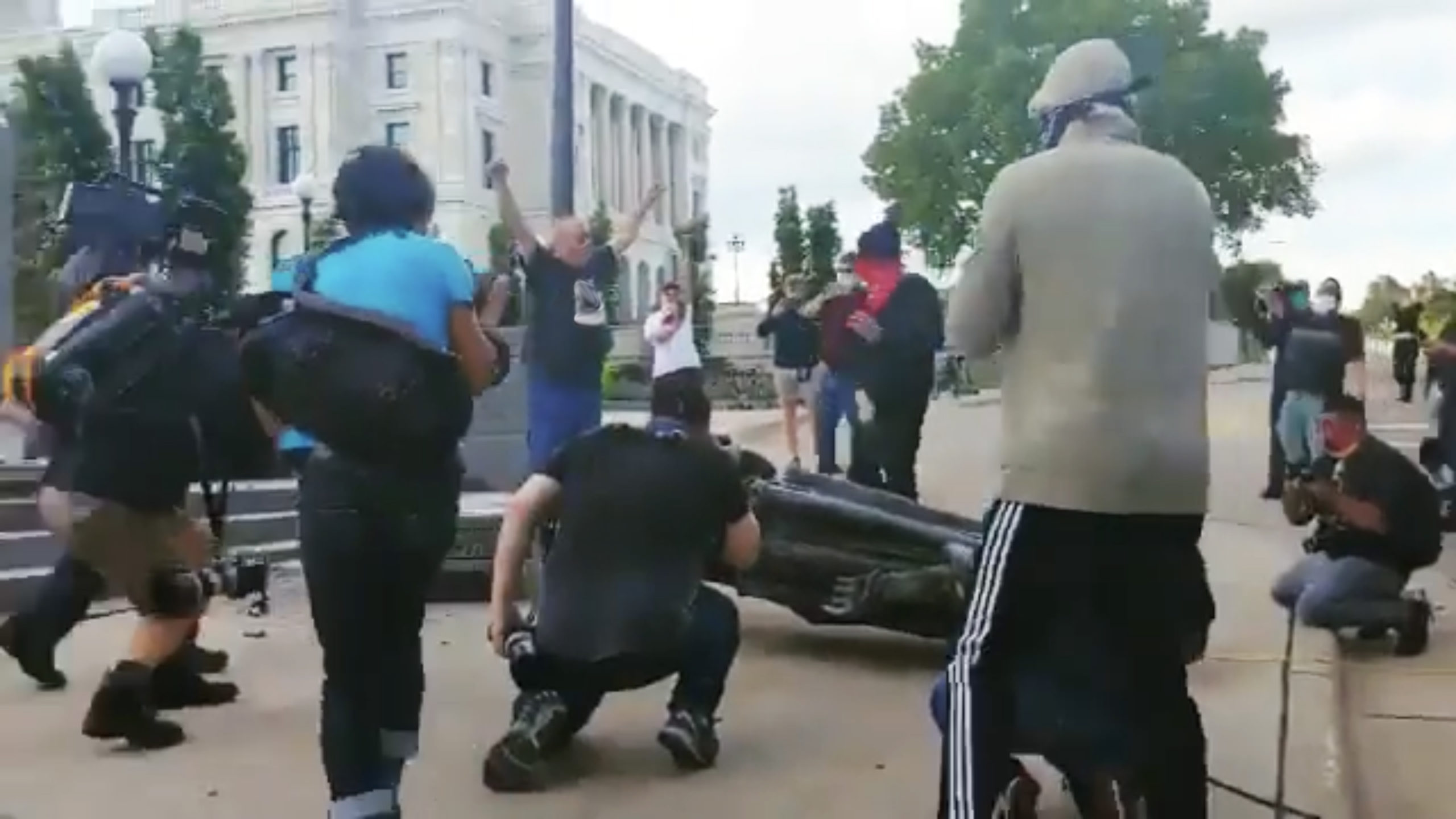 Statue of Christopher Columbus being toppled while group of people watch