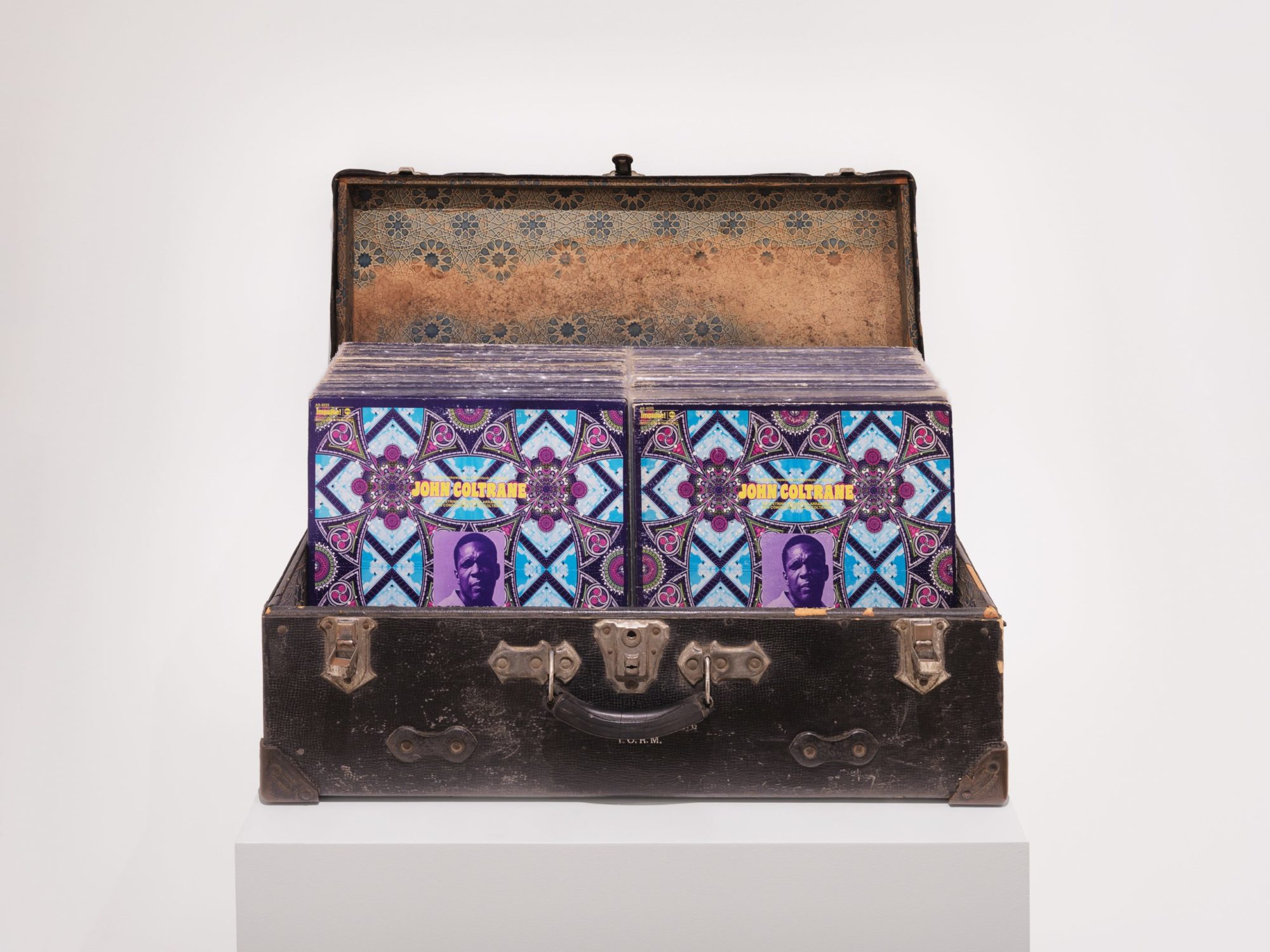 A vintage dark brown trunk opened to show a box adorned with mirrored images of John Coltrane's 