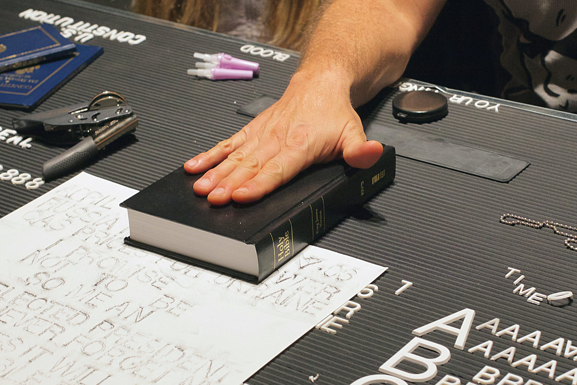 Close up of surface of black desk, Holy Bible rests on desk, a hand placed upon it