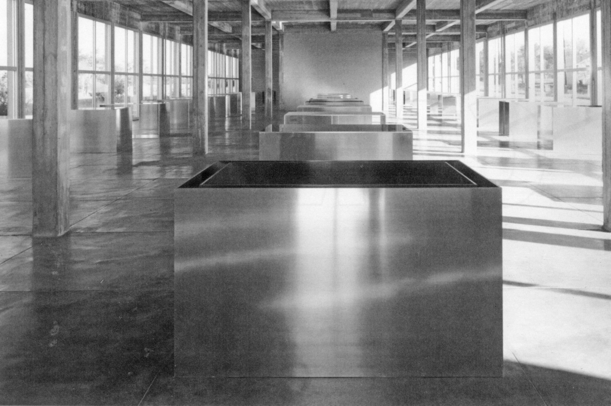 A row of reflective metal boxes centered and lined in a spacious room in between several small columns.