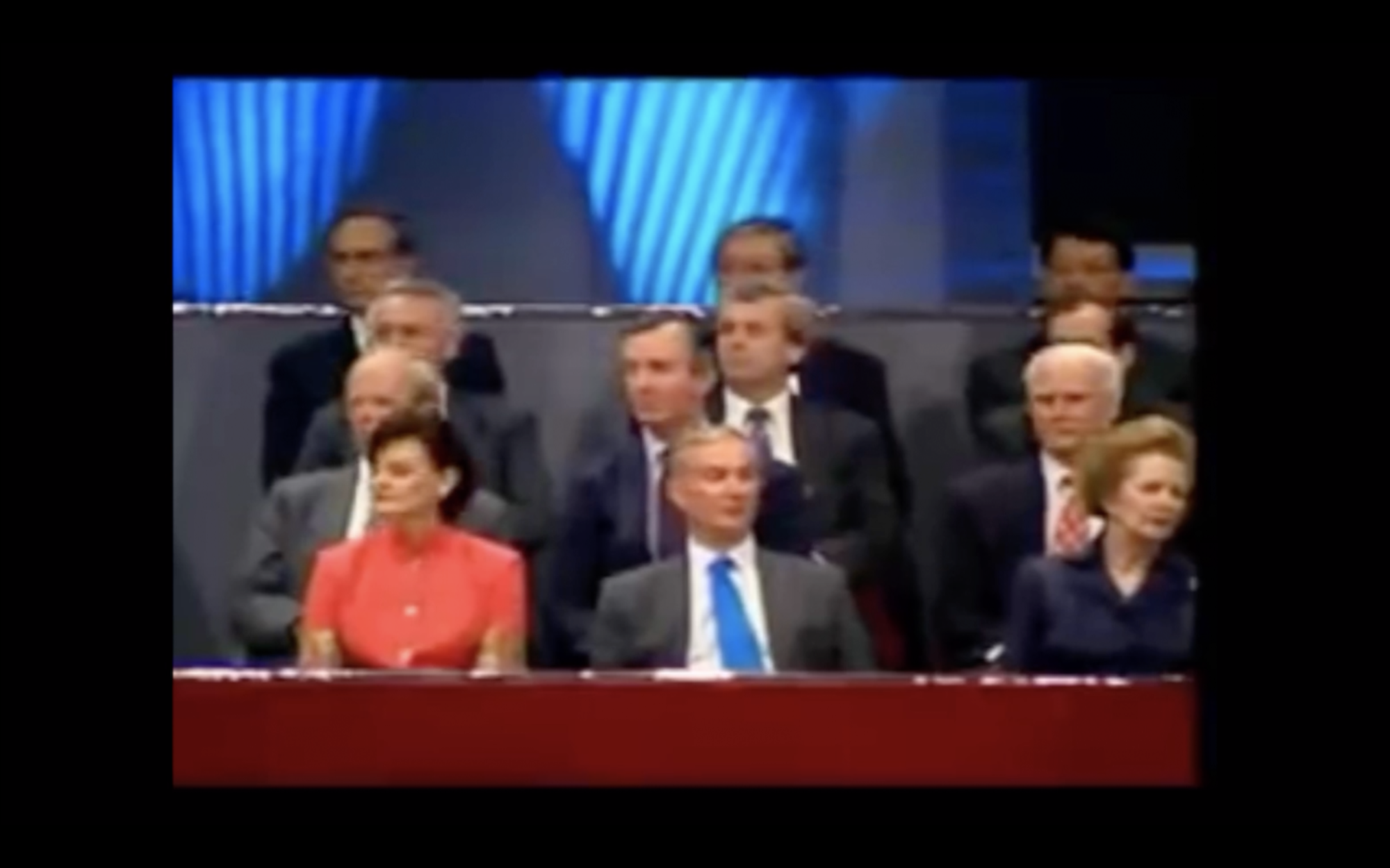 A grainy video still captured on Sia's phone of with various politicans sitting in three rows. In the front right hand side appears Margaret Thatcher
