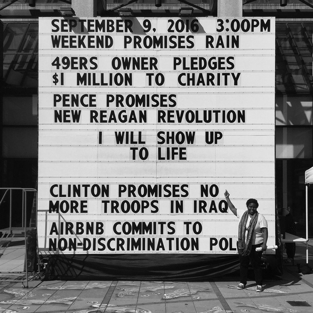 Black and white image of marquee with black letters spelling out date of September 9, 2016 and list of promises made by world political leaders and private citizens, woman stands below marquee and points upwards