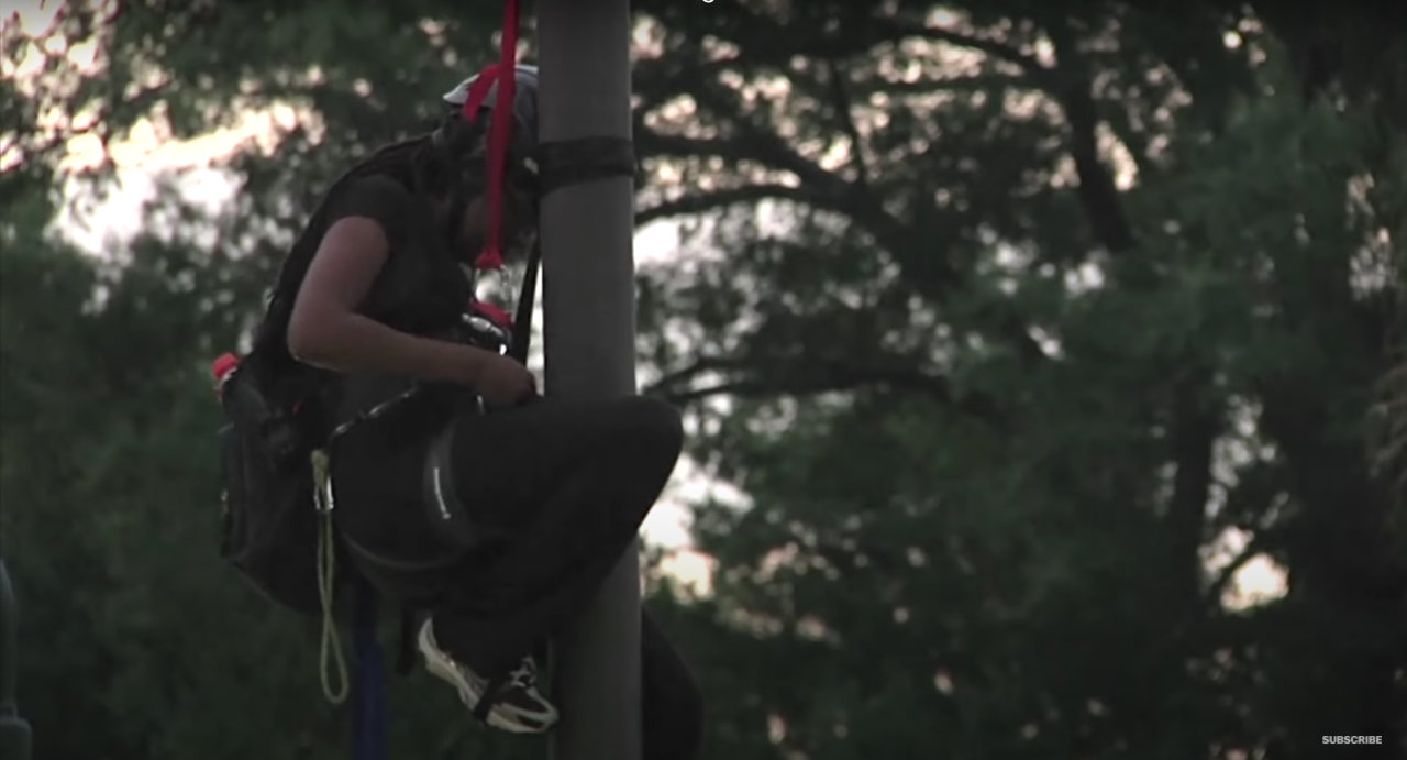 Close up image of a person, Bree Newsome, on a flag pole.