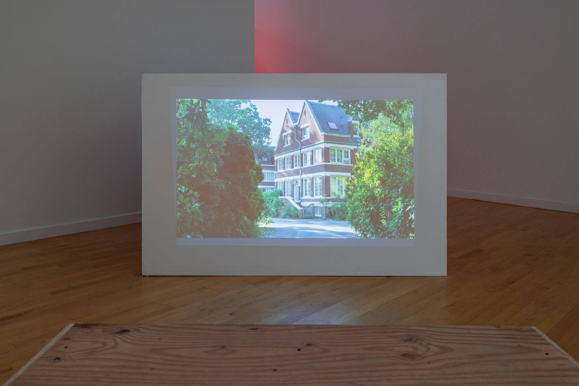 Large white panel in galery room with image of a colonial-style house surrounded by shrubbery projected upon it