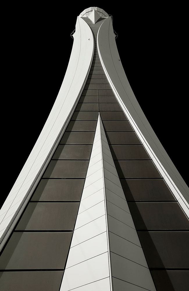 A grey and white tower is shot from below. It extends outward toward the bottom of the frame, and appears narrow at the top, with a combination.