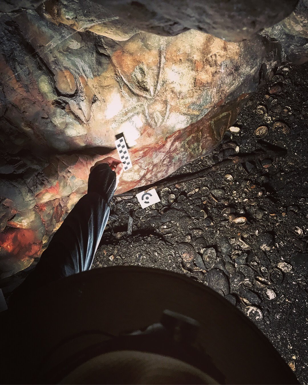 A figure holds a black and white checkered, rectangular object inside of a cave.