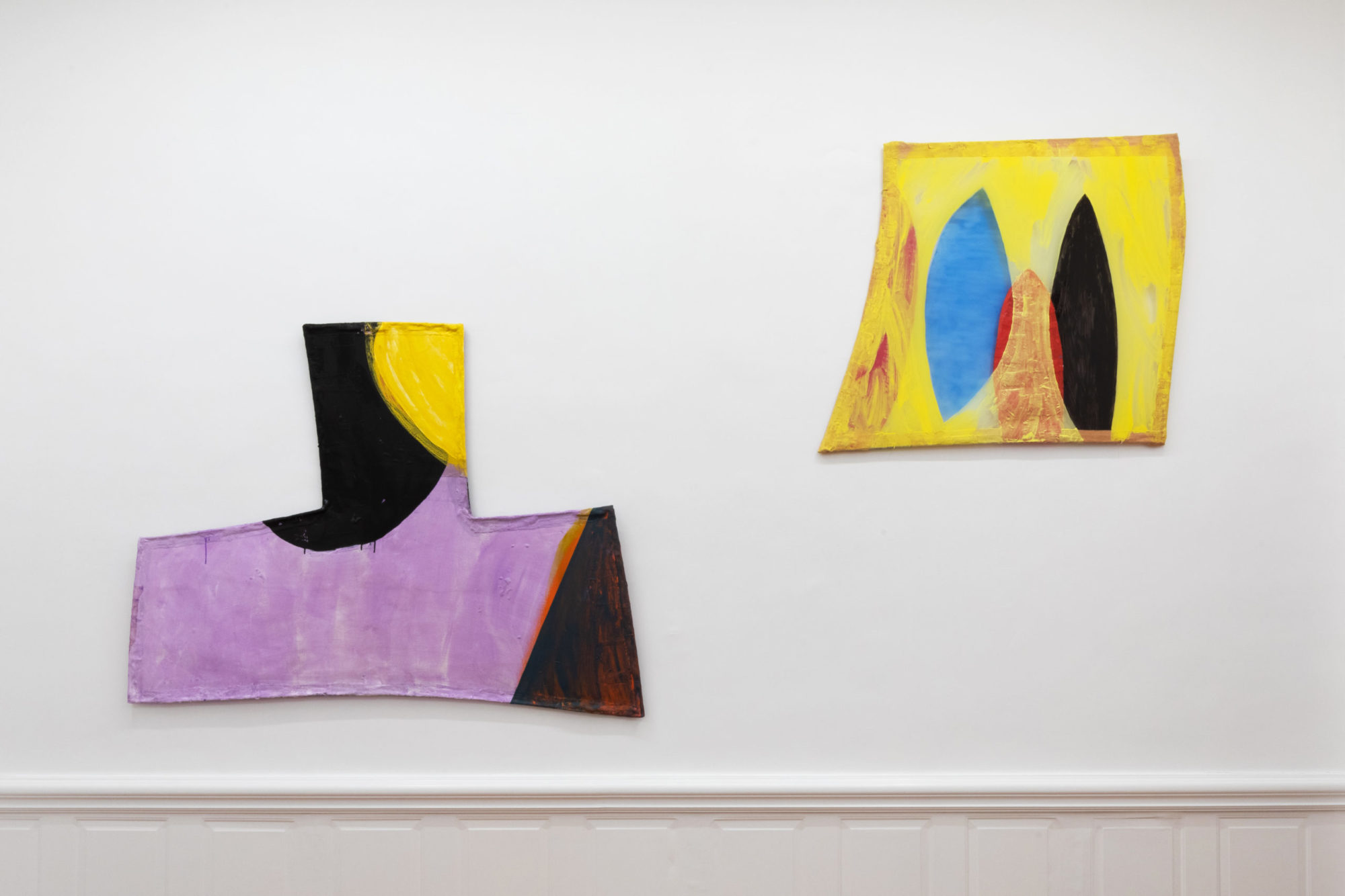 An installation view of Fabienne Lasserre's exhibition at TURN GALLERY in New York. Two pieces are mounted to the wall. They are angular in shape and feature bright purples and yellows.
