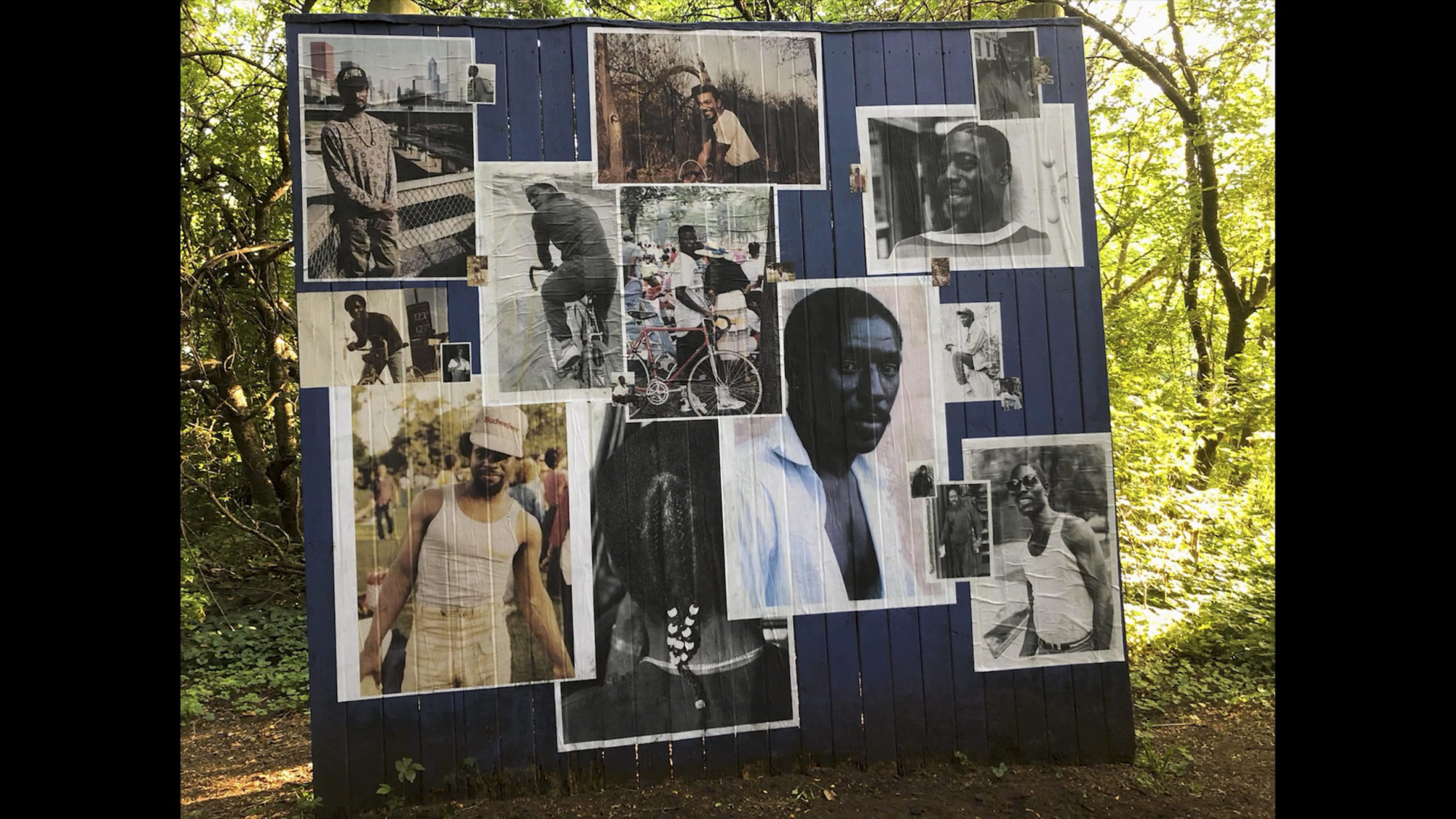An image of different photos of Black men collaged onto a blue wooden panel. The panel is in the woods.